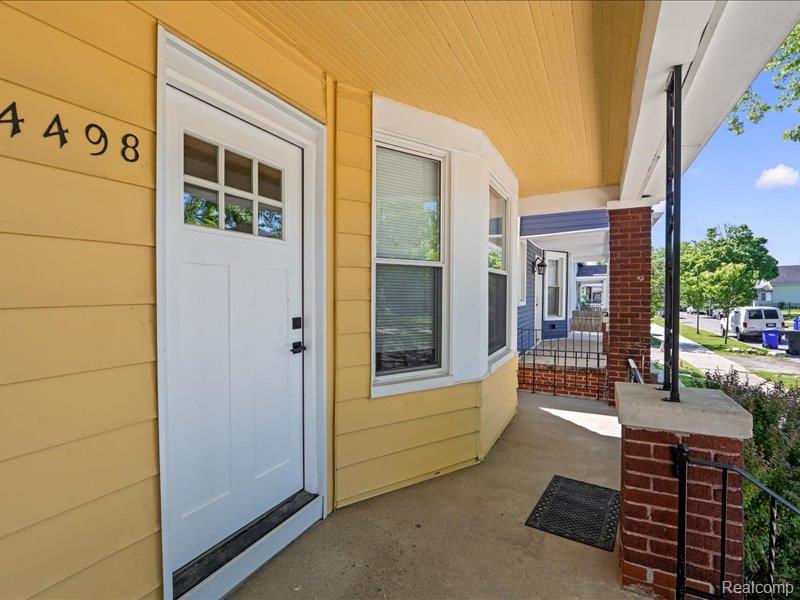 Covered front porch with yellow siding, white entry door, and brick columns.