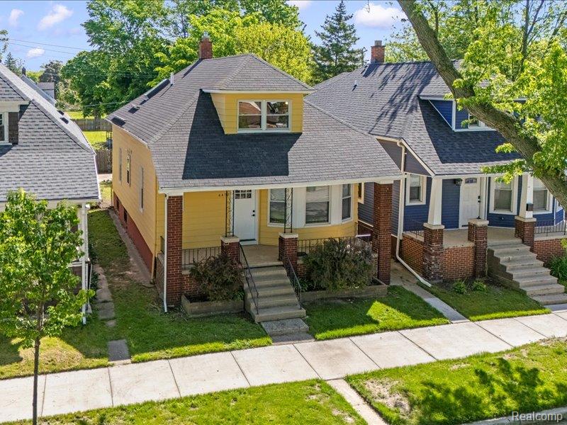 Yellow two-story house with a gray roof, dormer, and covered brick-column porch.
