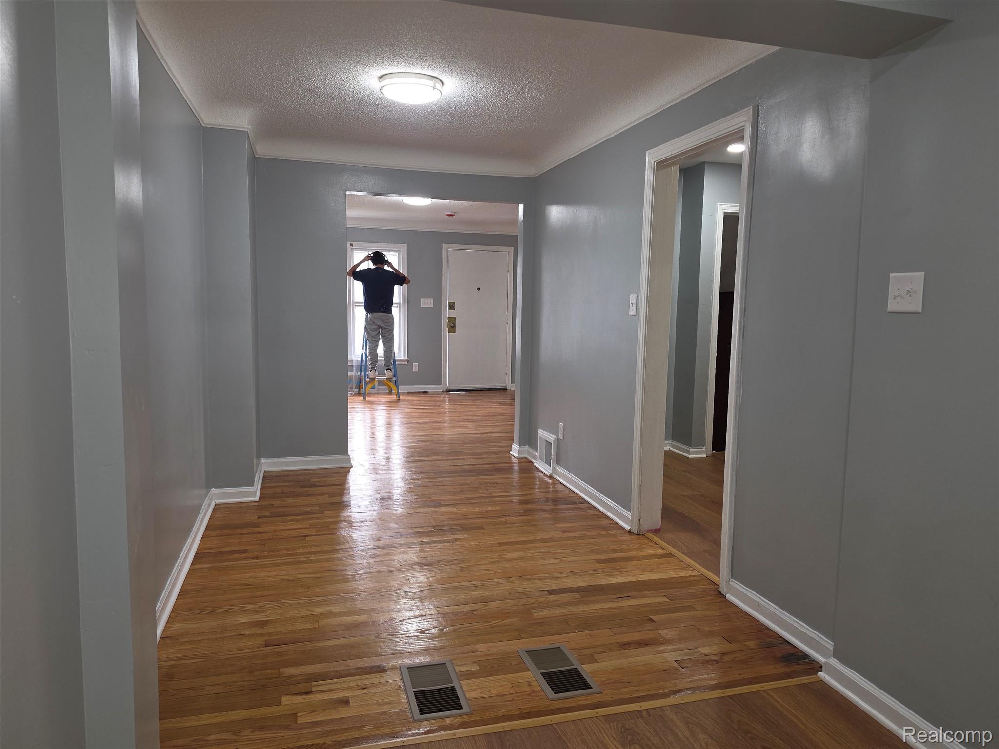 Hallway with polished hardwood floors, gray walls, and a person working at the far window.