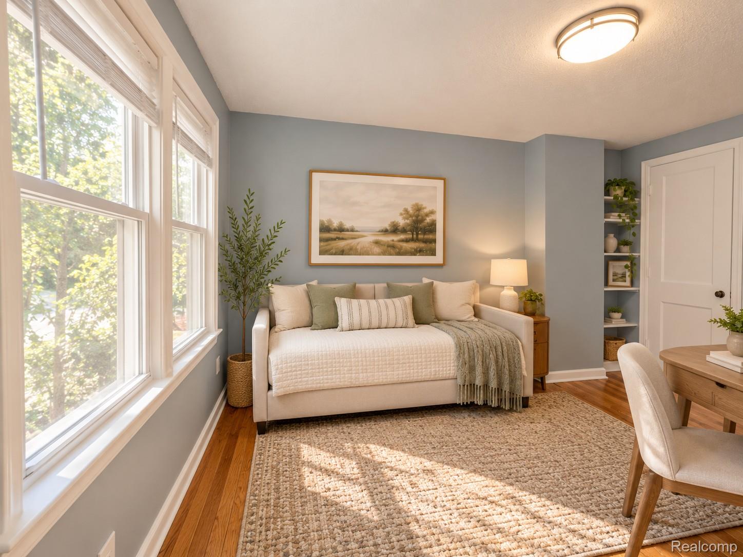 Staged sitting room with a cream sofa, large sunlit windows, and hardwood floors.