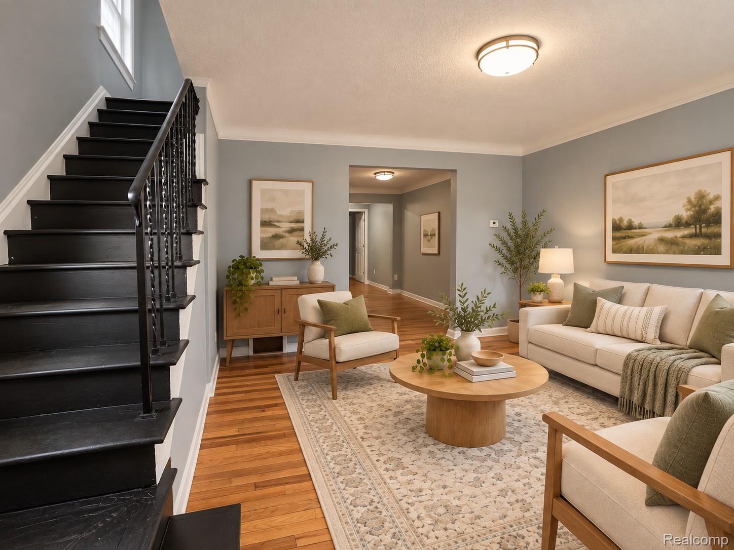 Staged living room with a black staircase, hardwood floors, and cream seating around a round coffee table.