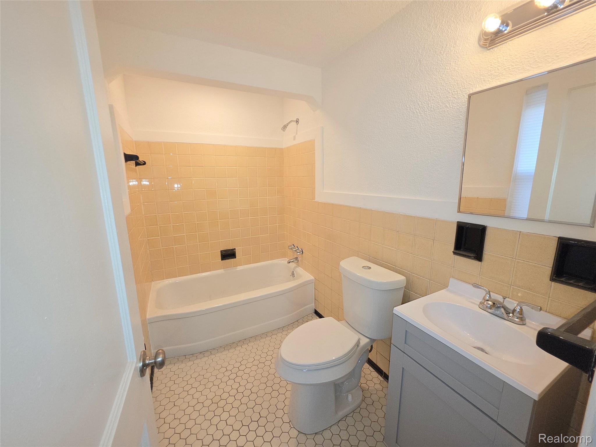 Bathroom with peach tile around a bathtub, a toilet, and a gray vanity.