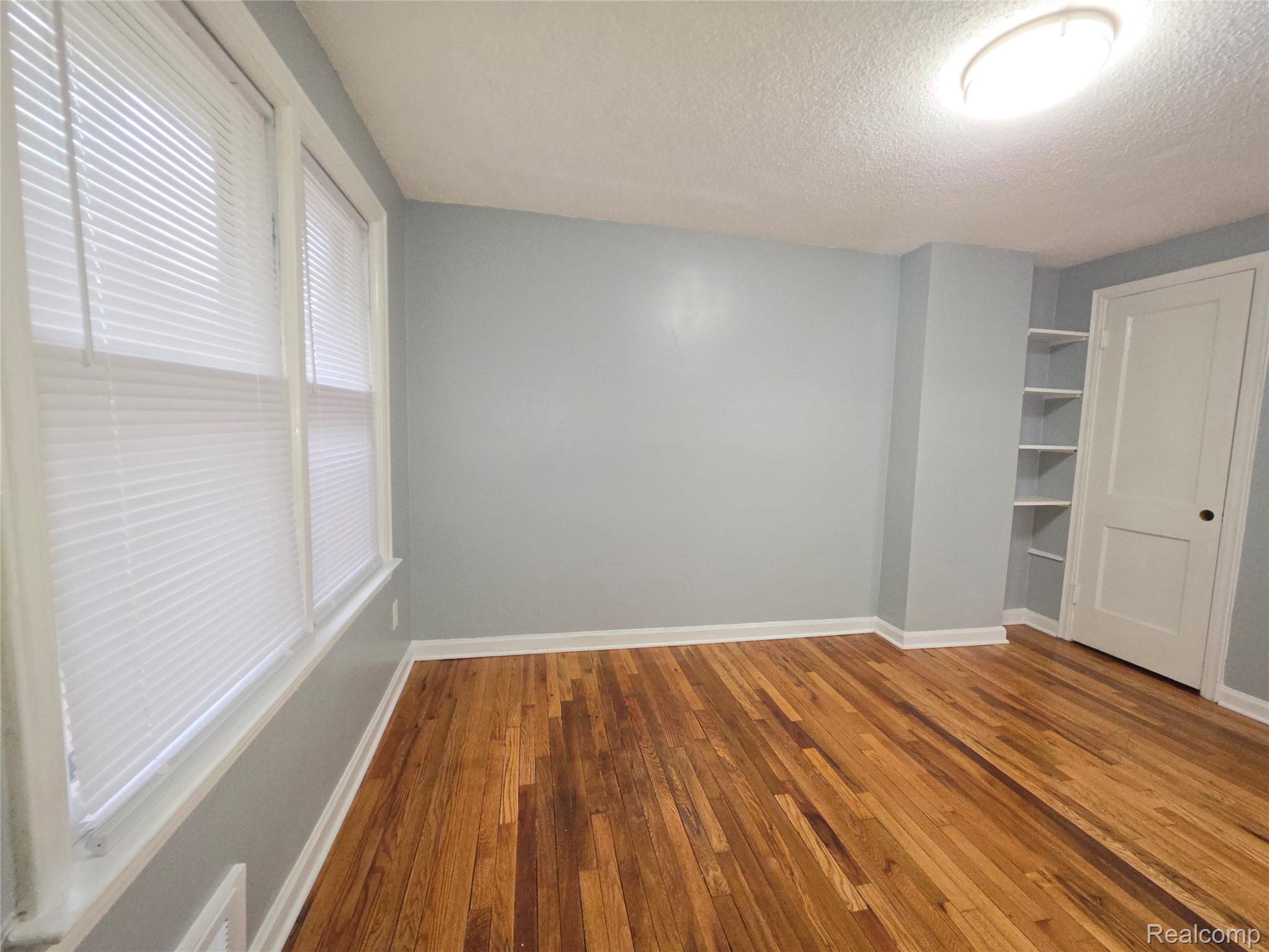 Empty bedroom with hardwood floors, two blinded windows, and built-in closet shelves.