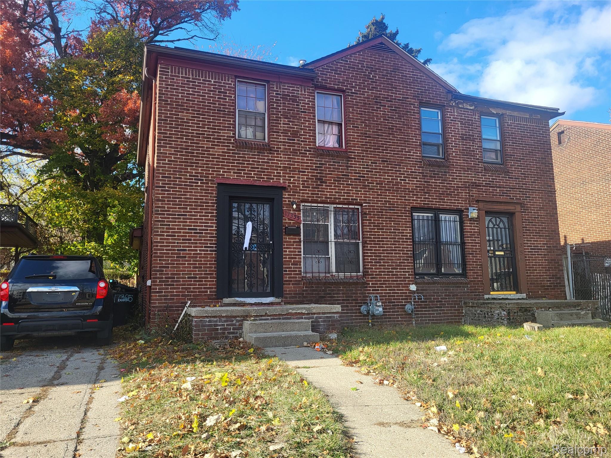 Two-story red-brick home with barred windows, two front entrances, and a tree-lined driveway.