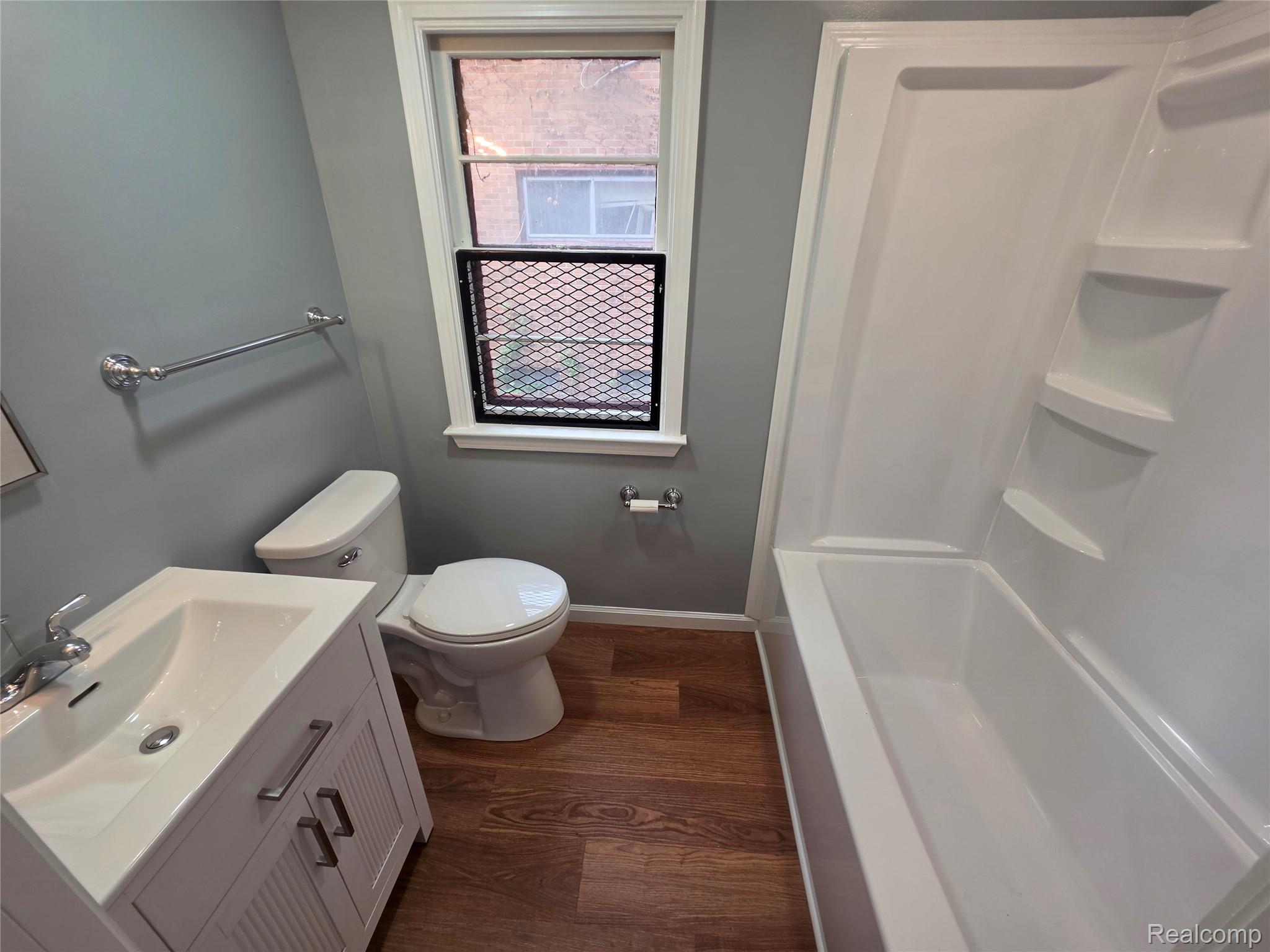 Bathroom with gray walls, a white vanity and tub-shower, and dark wood-look flooring.