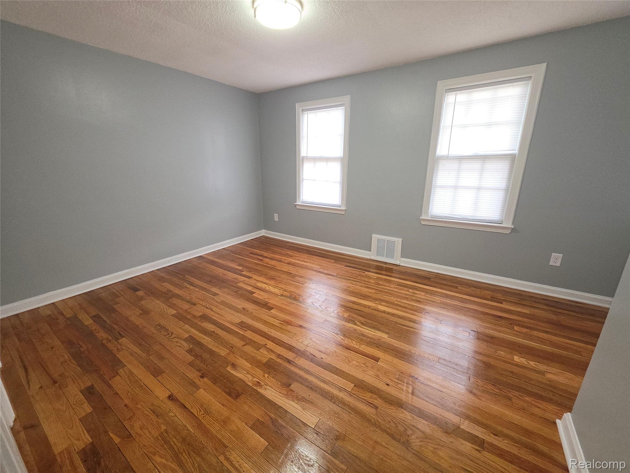 Empty room with gray walls, two windows, and polished hardwood floors.