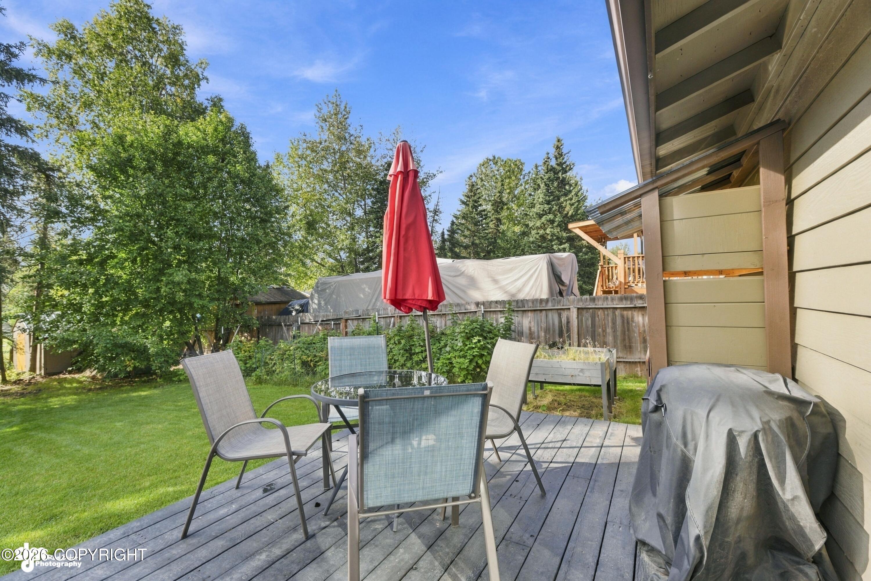 Backyard deck with patio seating and a closed red umbrella beside a fenced lawn.