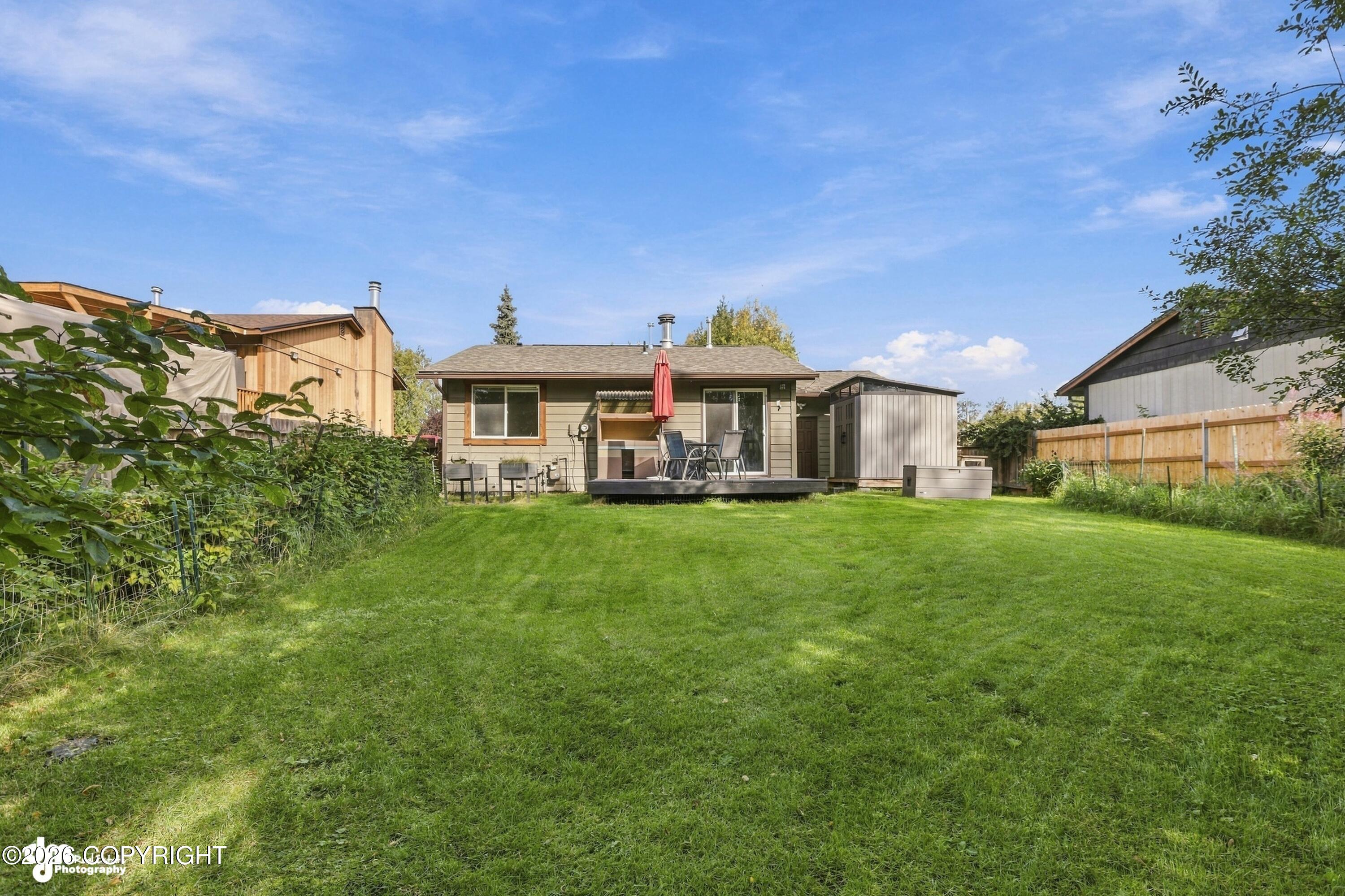 Rear of a single-story home with a spacious lawn, deck seating, red umbrella, and backyard shed.