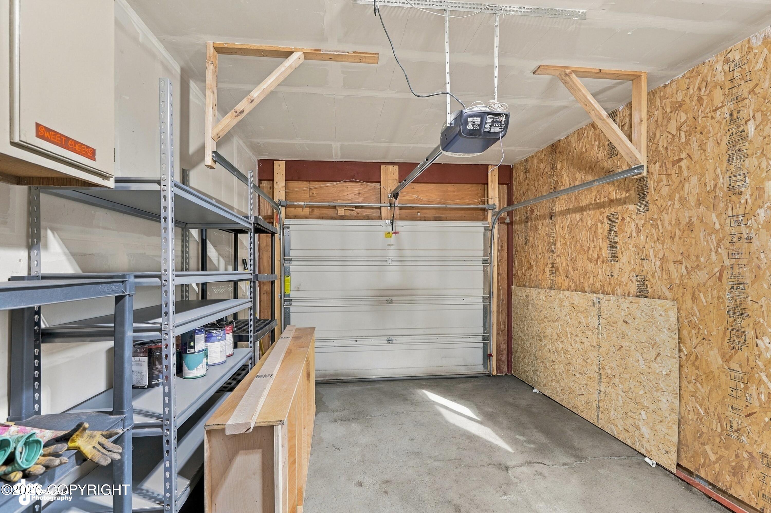 Garage with metal storage shelving, a workbench, and exposed OSB wall sheathing.