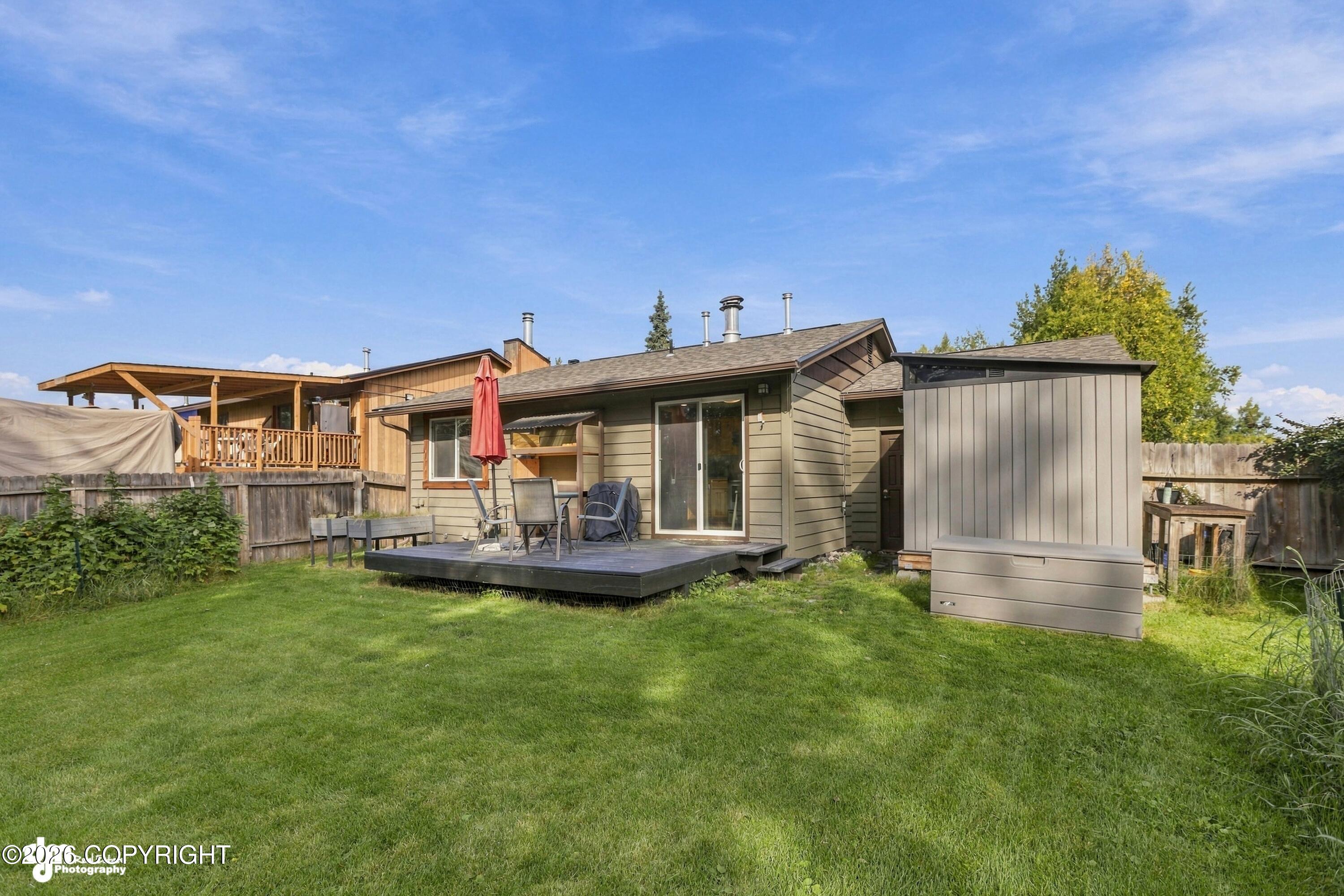 House rear with a raised patio deck, outdoor seating, and a broad green lawn.