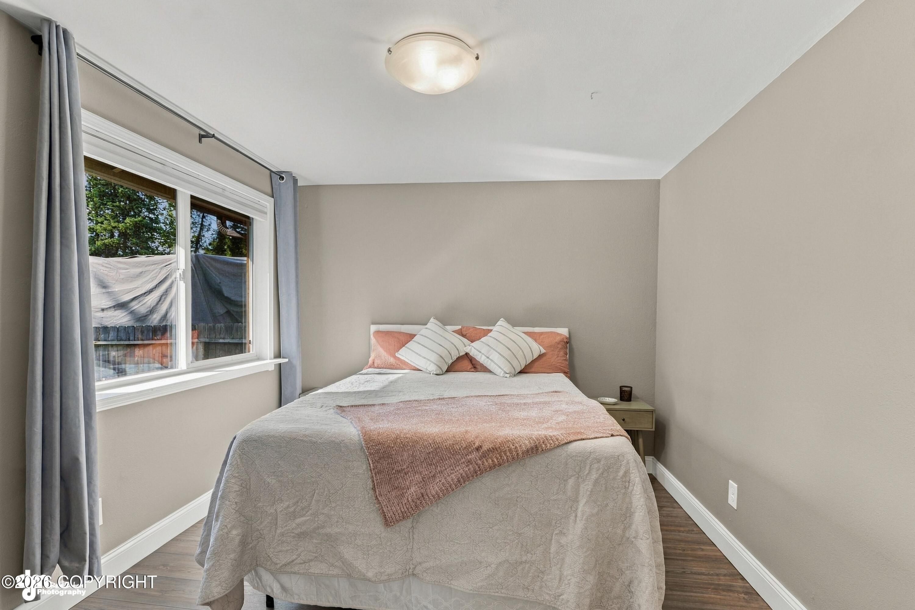 Staged bedroom with a gray-and-rose bed beside a large curtained window.