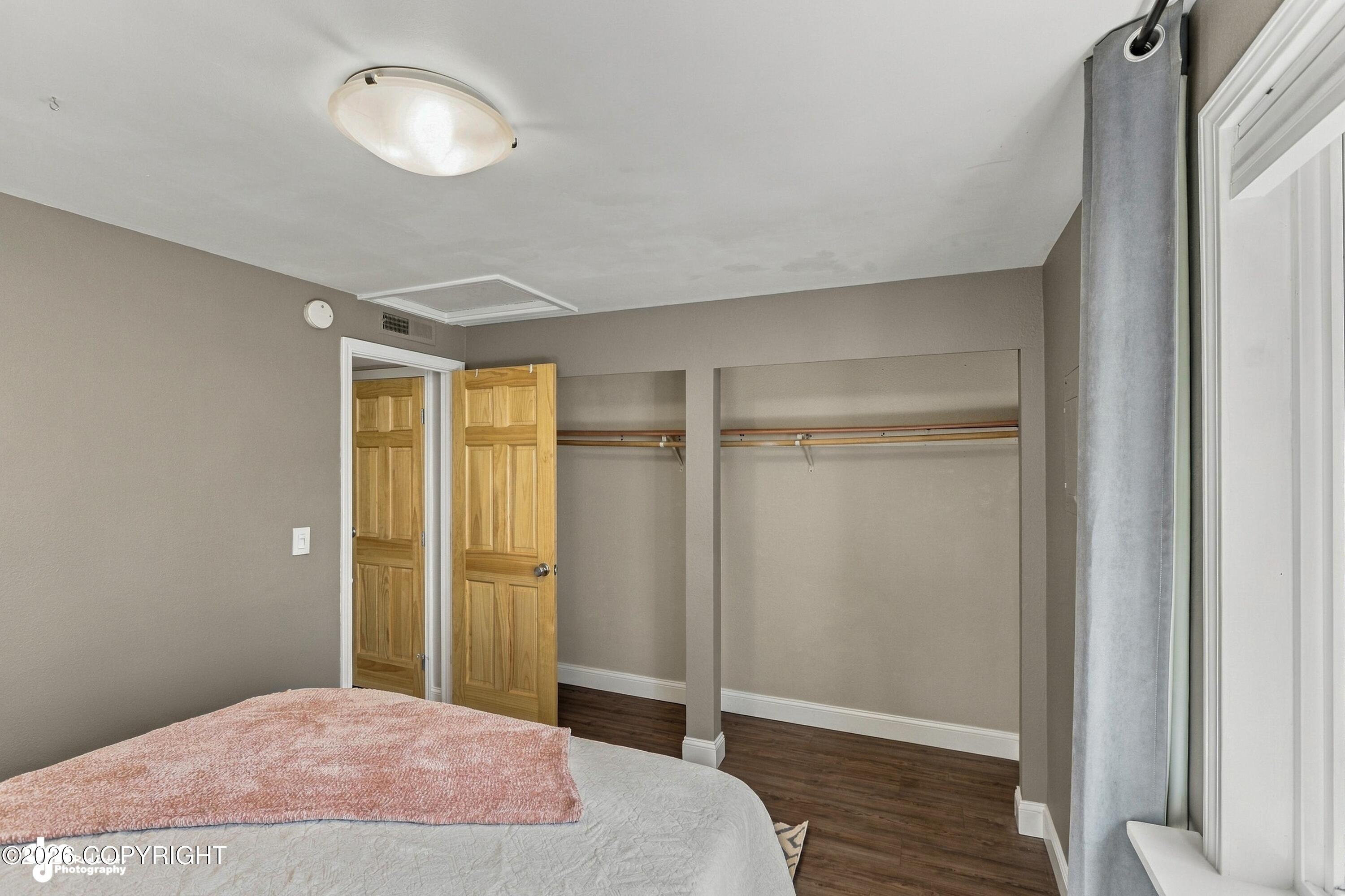 Bedroom with open closet, dark wood flooring, and a bed with a pink throw.