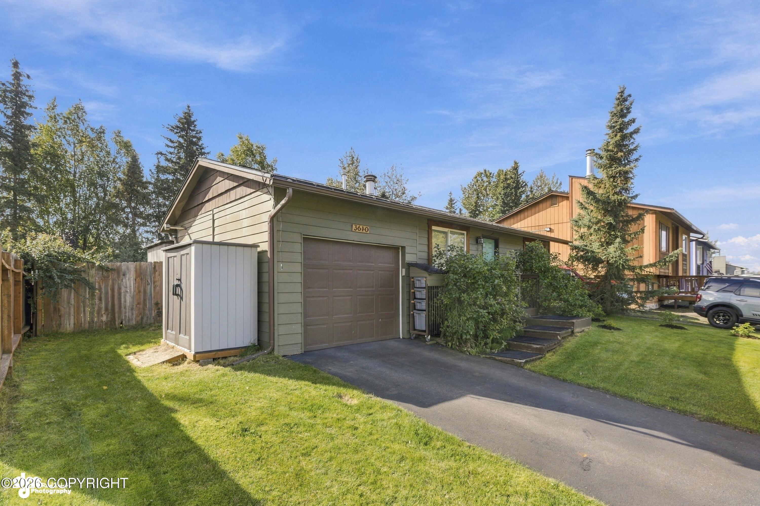 Green-sided home with a large garage, white shed, and paved driveway.