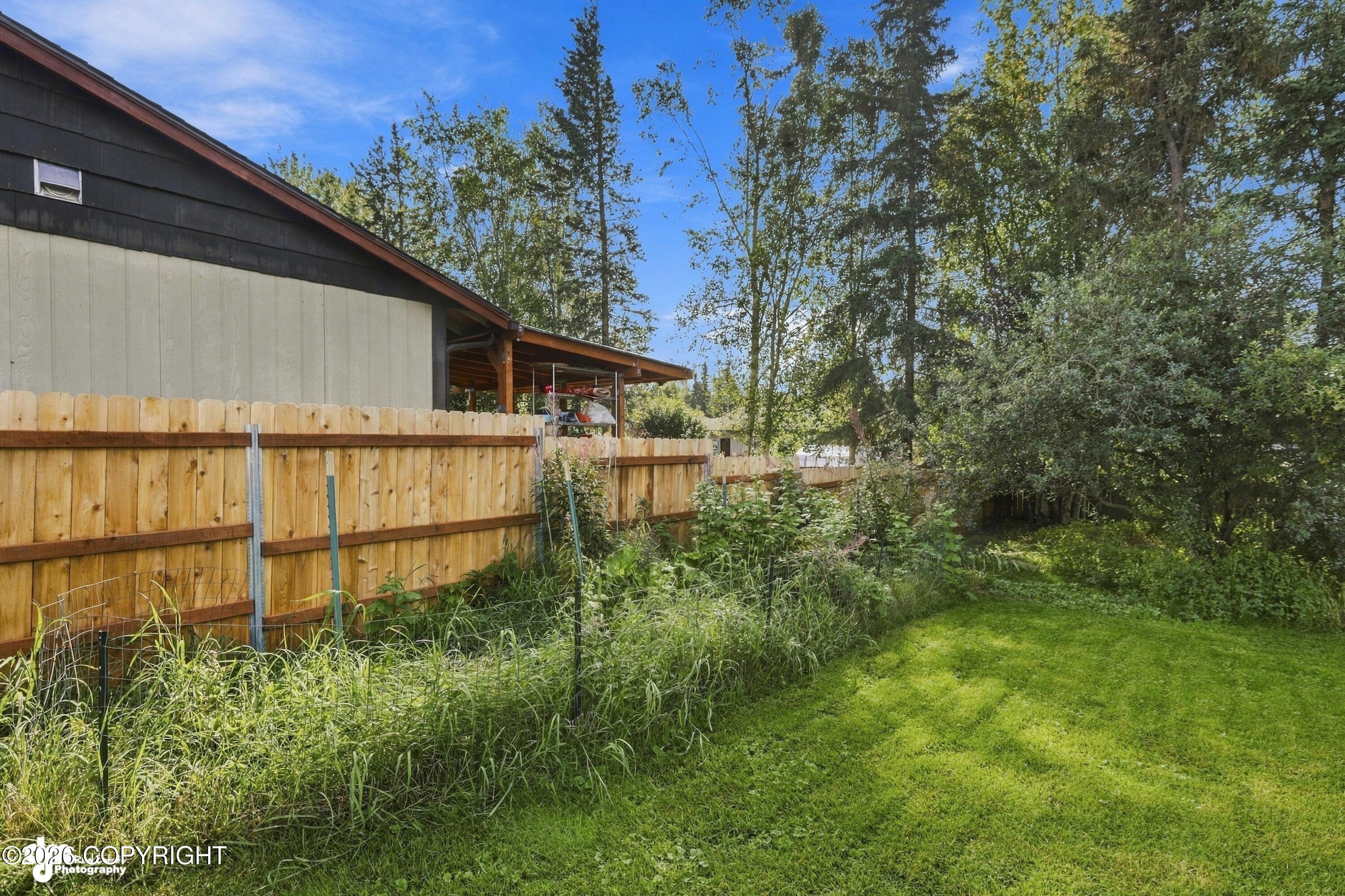 Fenced side yard with a covered patio, mature trees, and a broad green lawn.