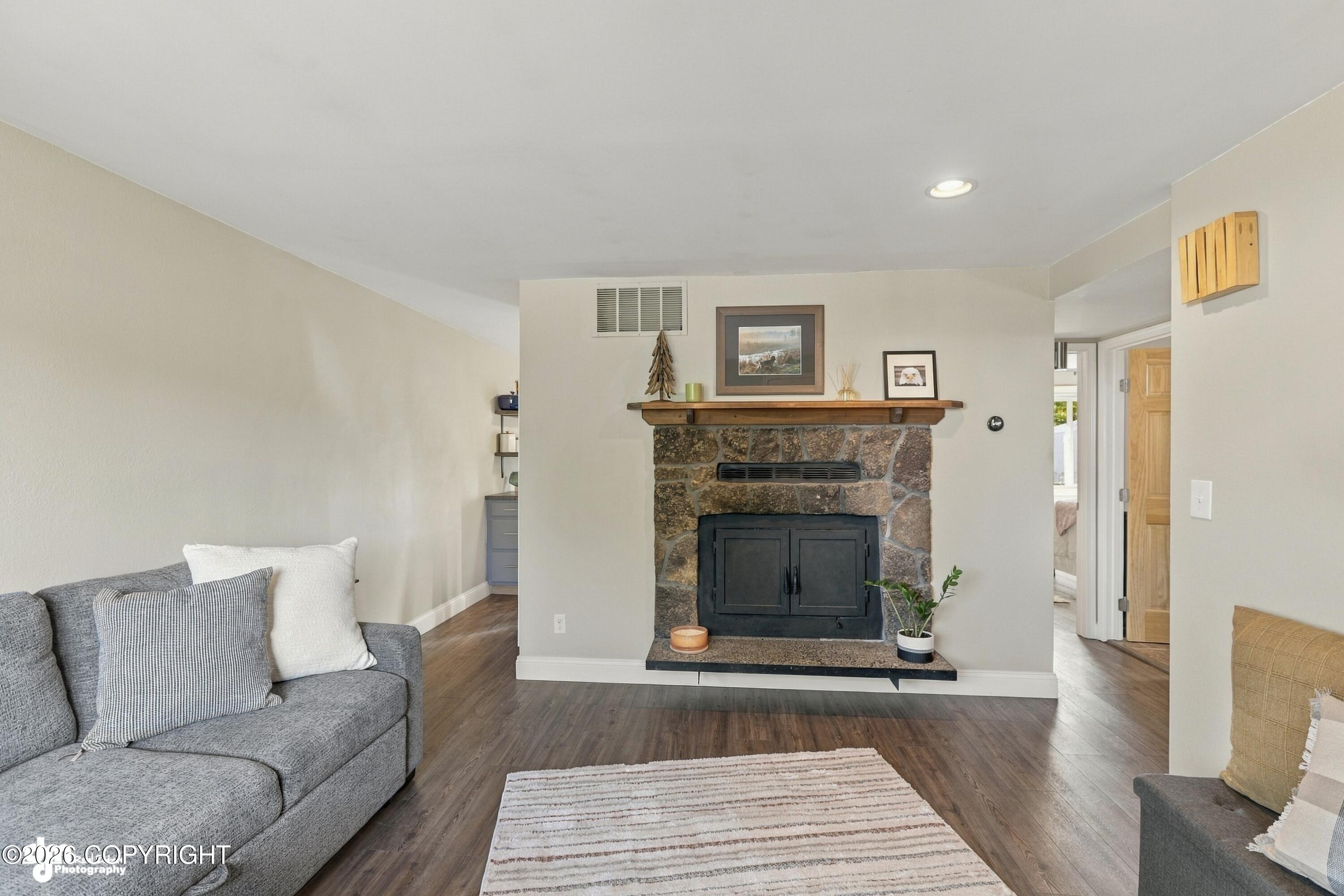 Living room with a stone fireplace, wooden mantel, and gray sectional sofa.