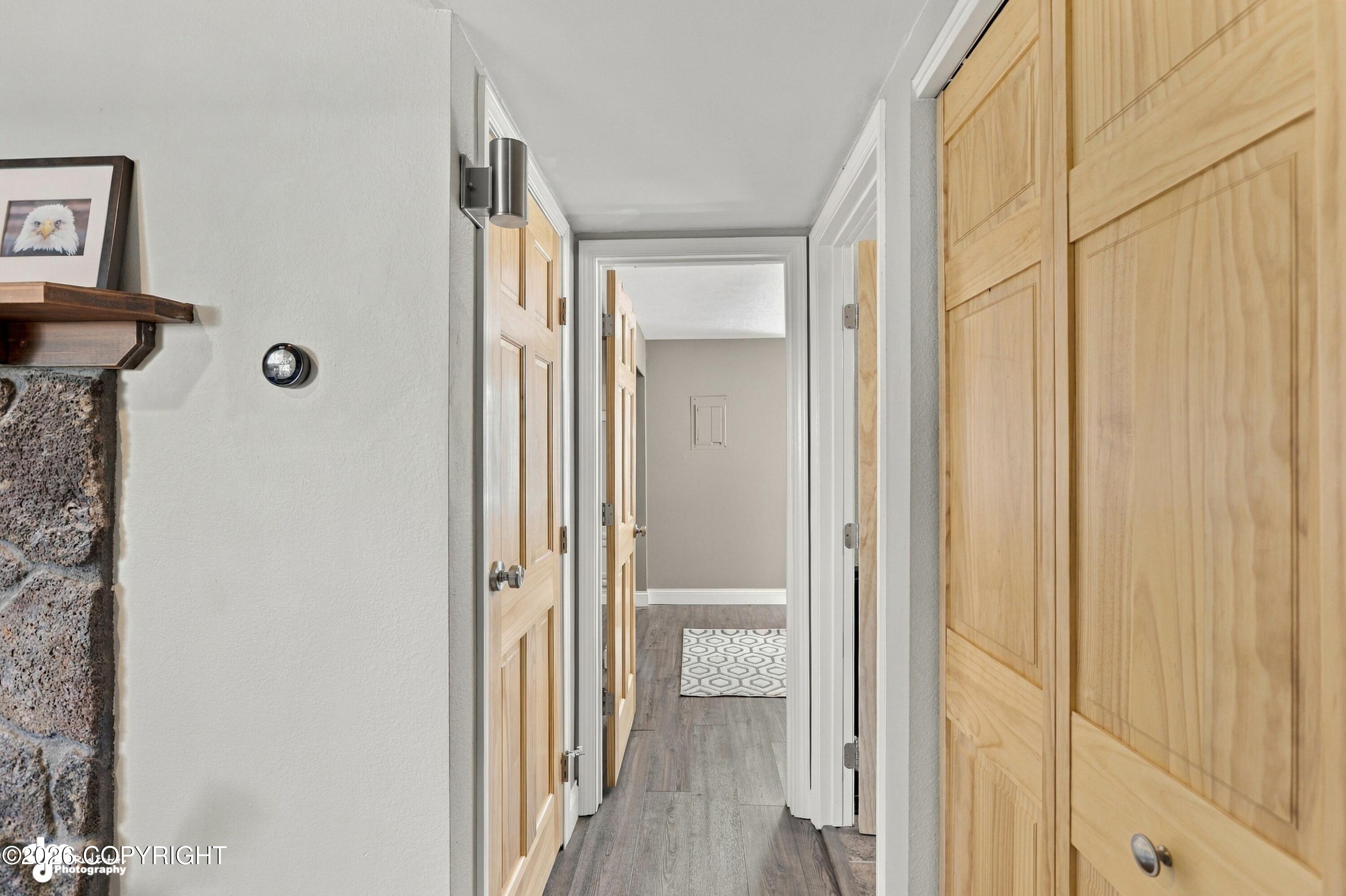 Hallway with light wood paneled doors, gray flooring, and a patterned rug at the far end.