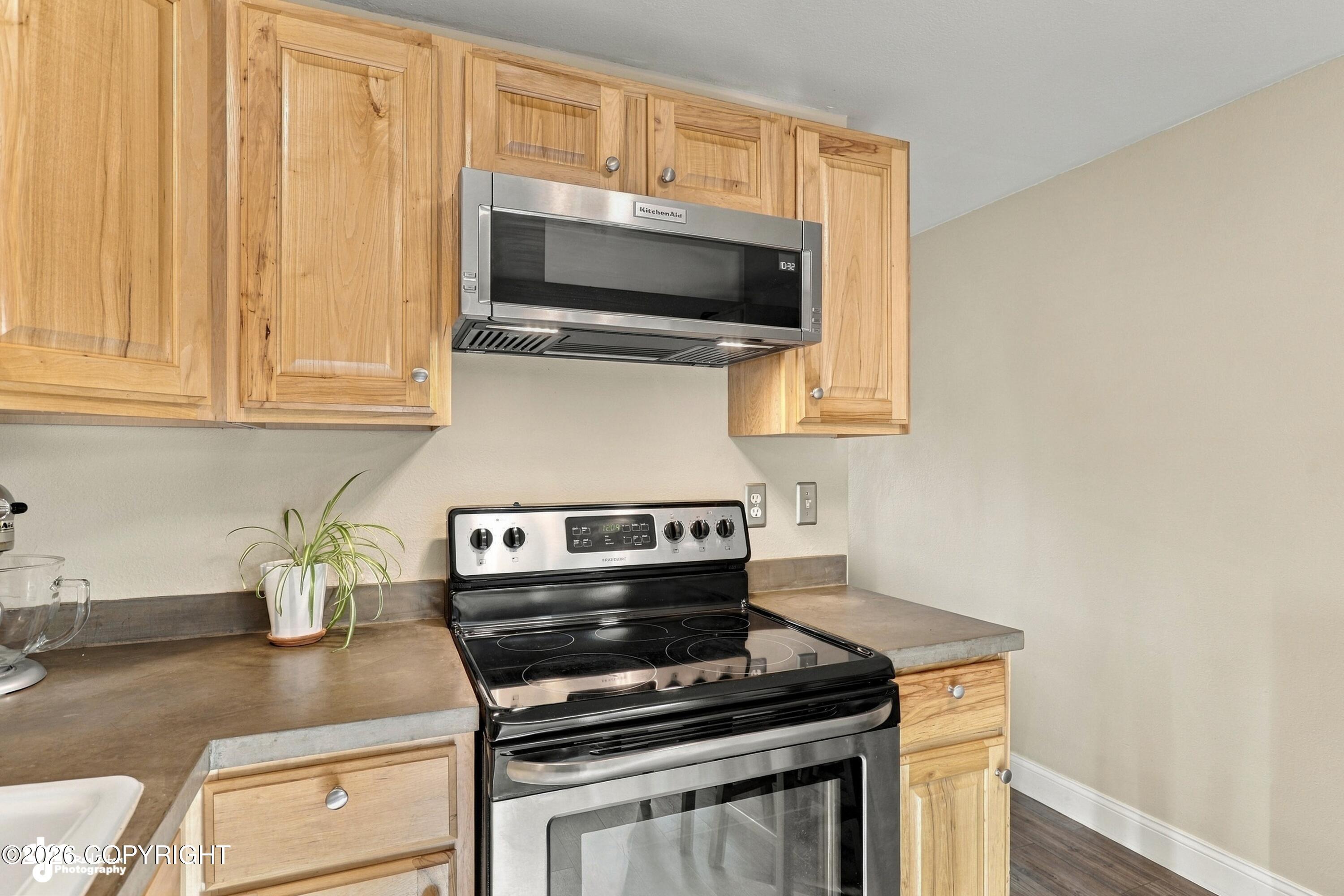 Kitchen with natural wood cabinets, electric range, stainless microwave, and brown countertops.