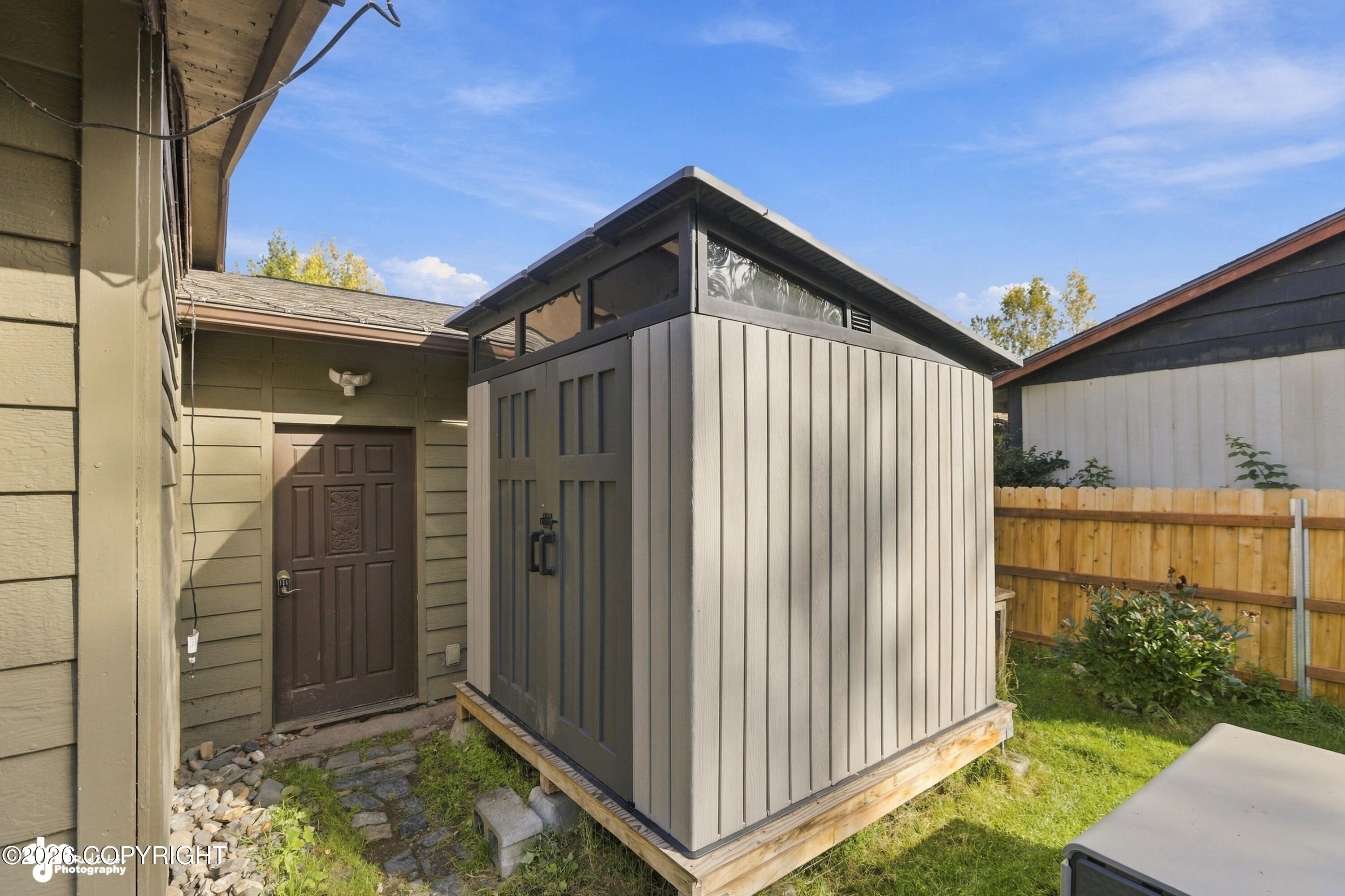Backyard with a modern gray outbuilding beside the home's brown entry door.