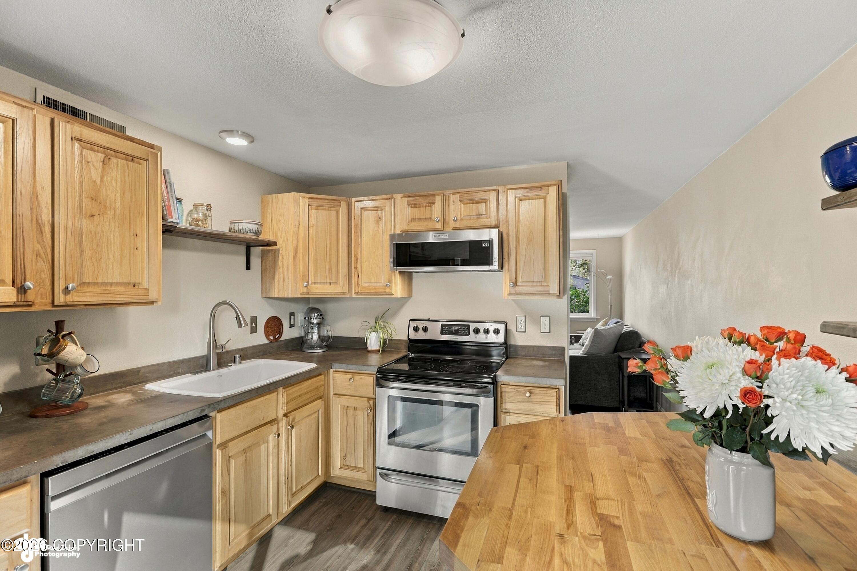 Kitchen with light wood cabinets, stainless steel appliances, and a butcher-block island with flowers.