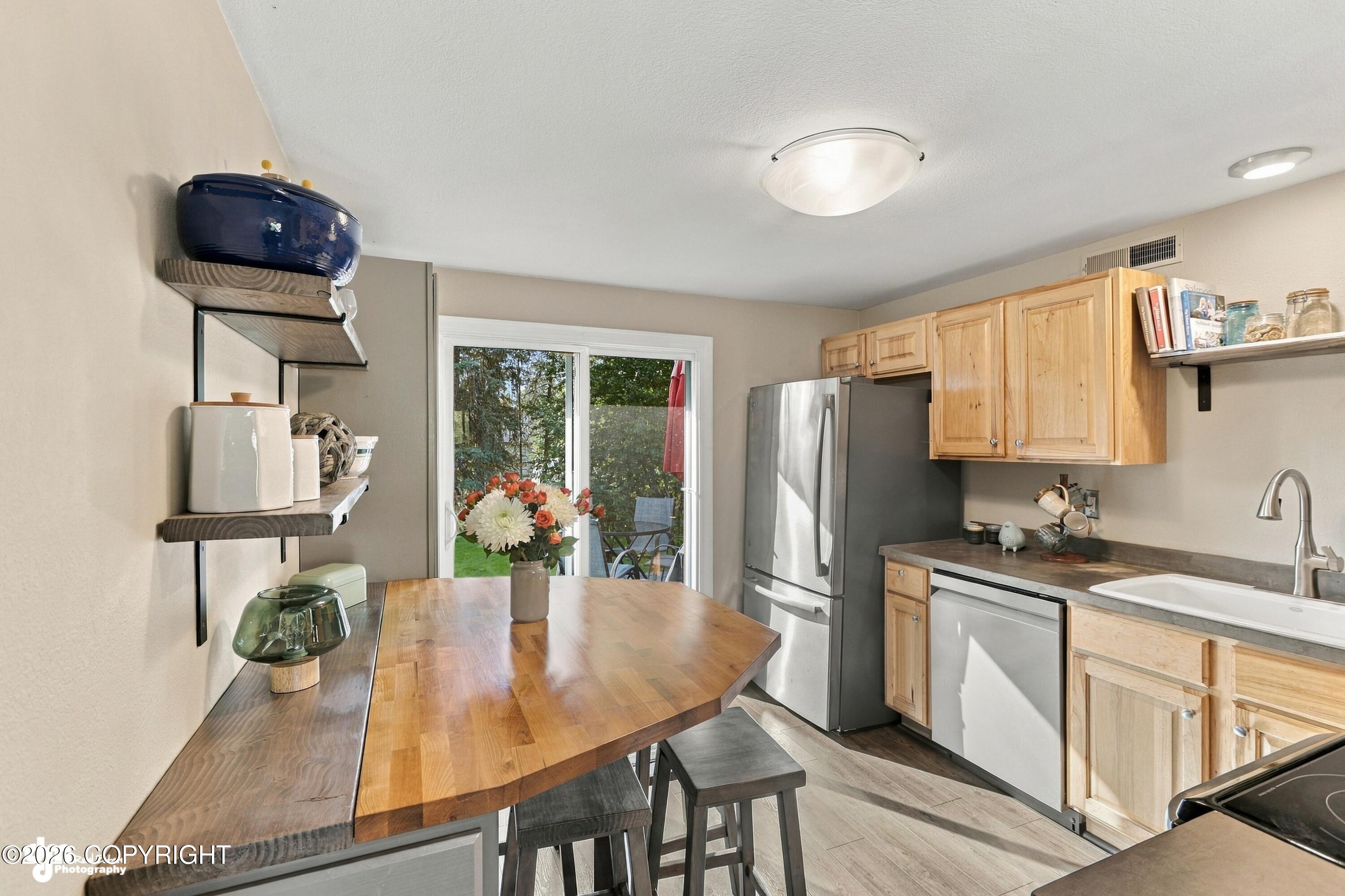 Kitchen with light wood cabinets, stainless steel appliances, and a butcher-block table beside sliding glass doors.