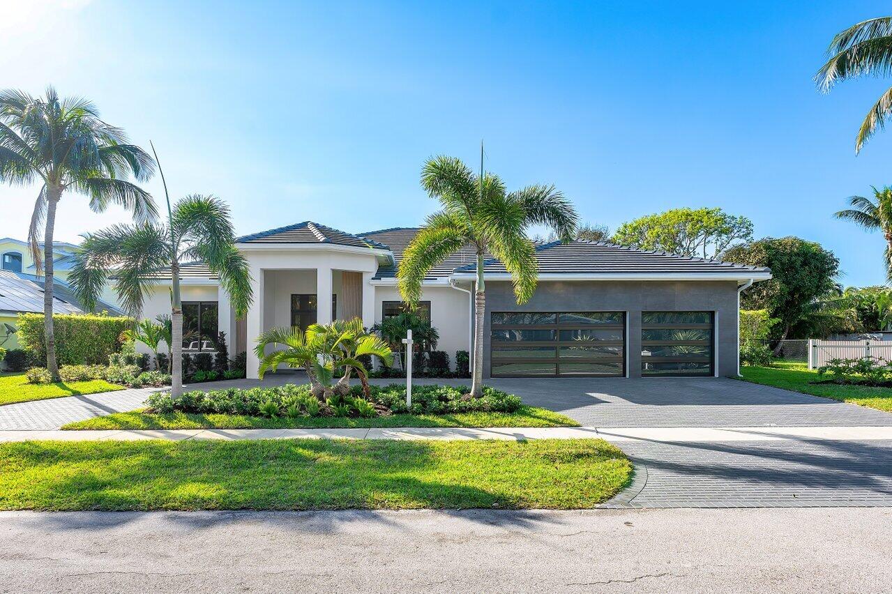 Modern single-story home with gray garage doors, palm trees, and a landscaped front yard.
