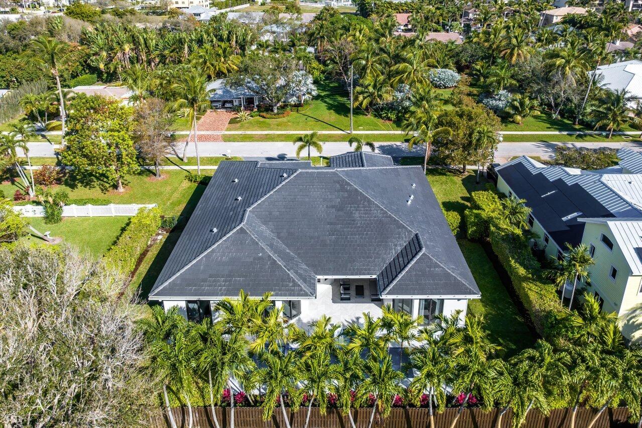 Aerial view of a single-story home with a dark gray roof, palm trees, and lush landscaping.