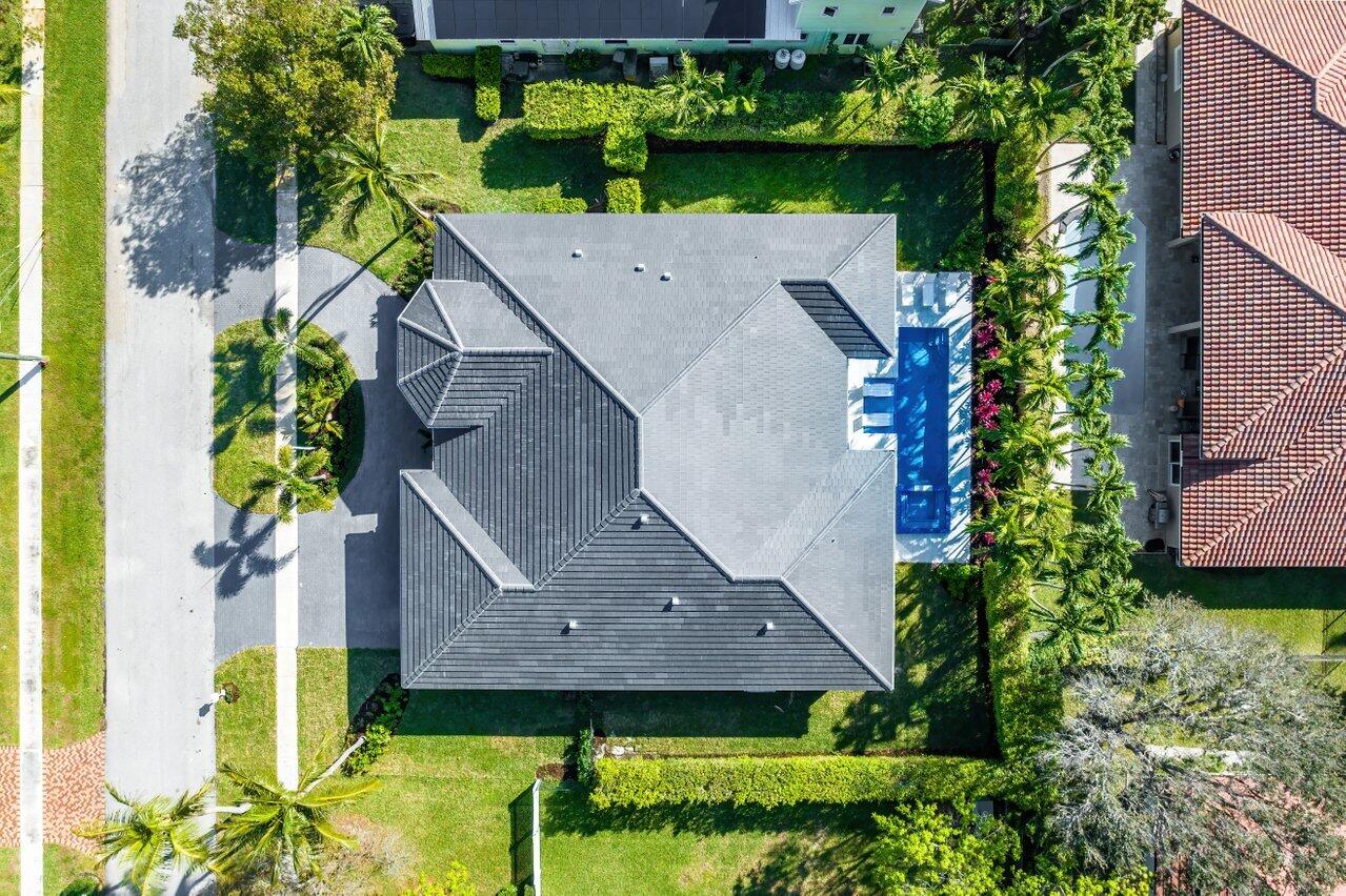 Aerial view of a home with a gray roof, landscaped yard, and rectangular blue pool.
