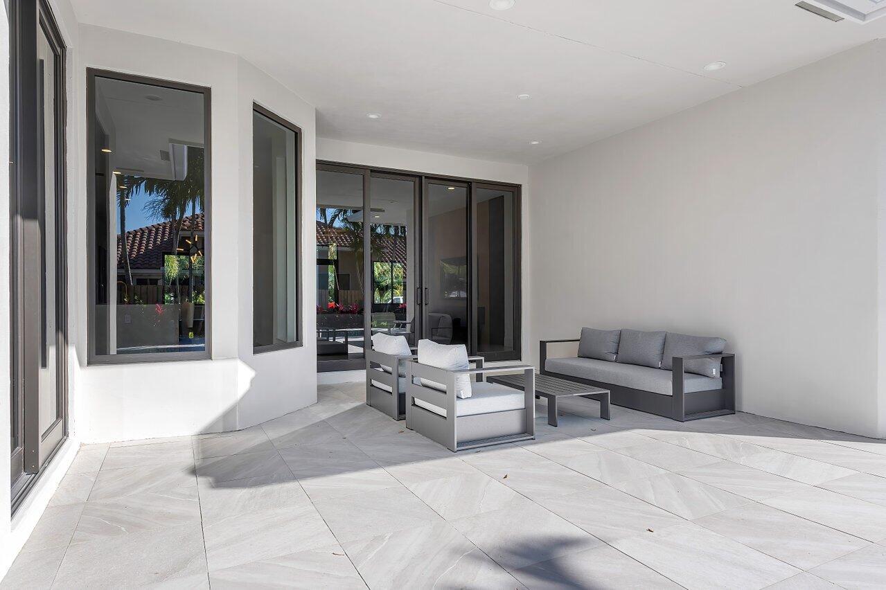 Covered patio with modern gray seating, pale stone tiles, and dark-framed glass doors.