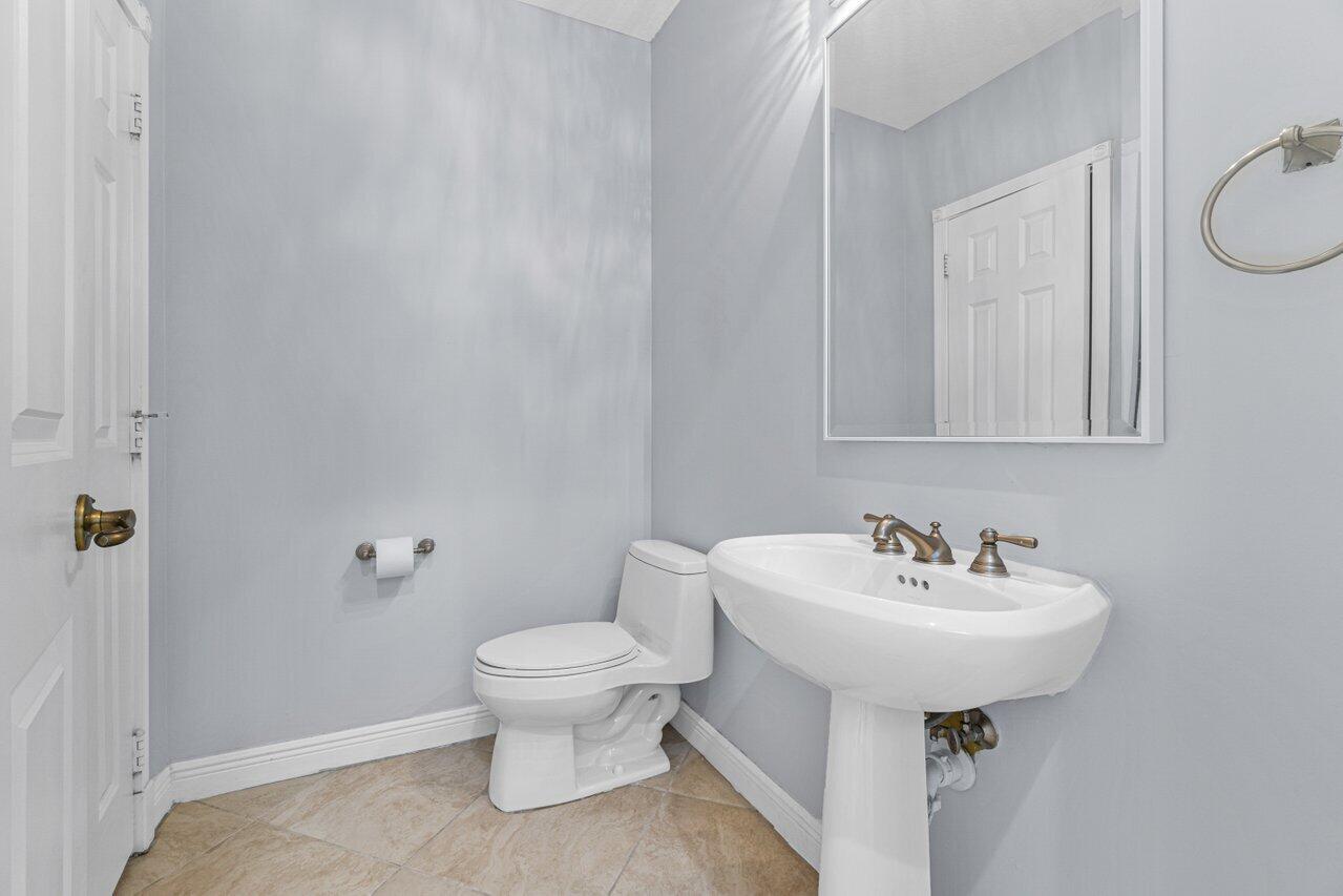 Bathroom with a pedestal sink, large wall mirror, and beige tile floor.