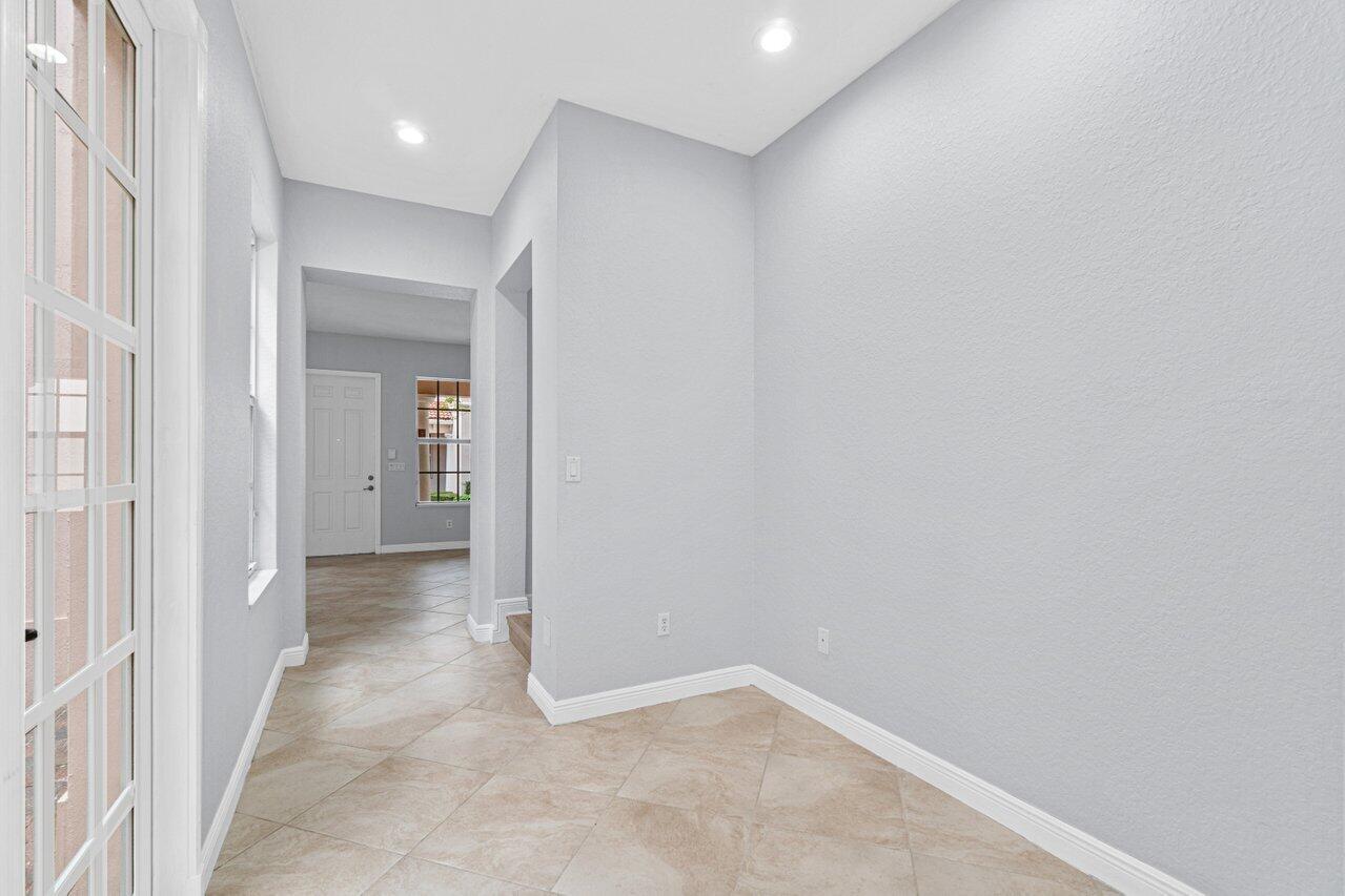 Vacant foyer with beige tile floors, tall windows, and the front door at the end of the hall.