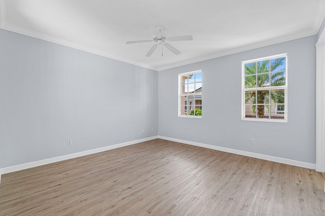 Empty bedroom with light wood-look floors, two windows, and a ceiling fan.