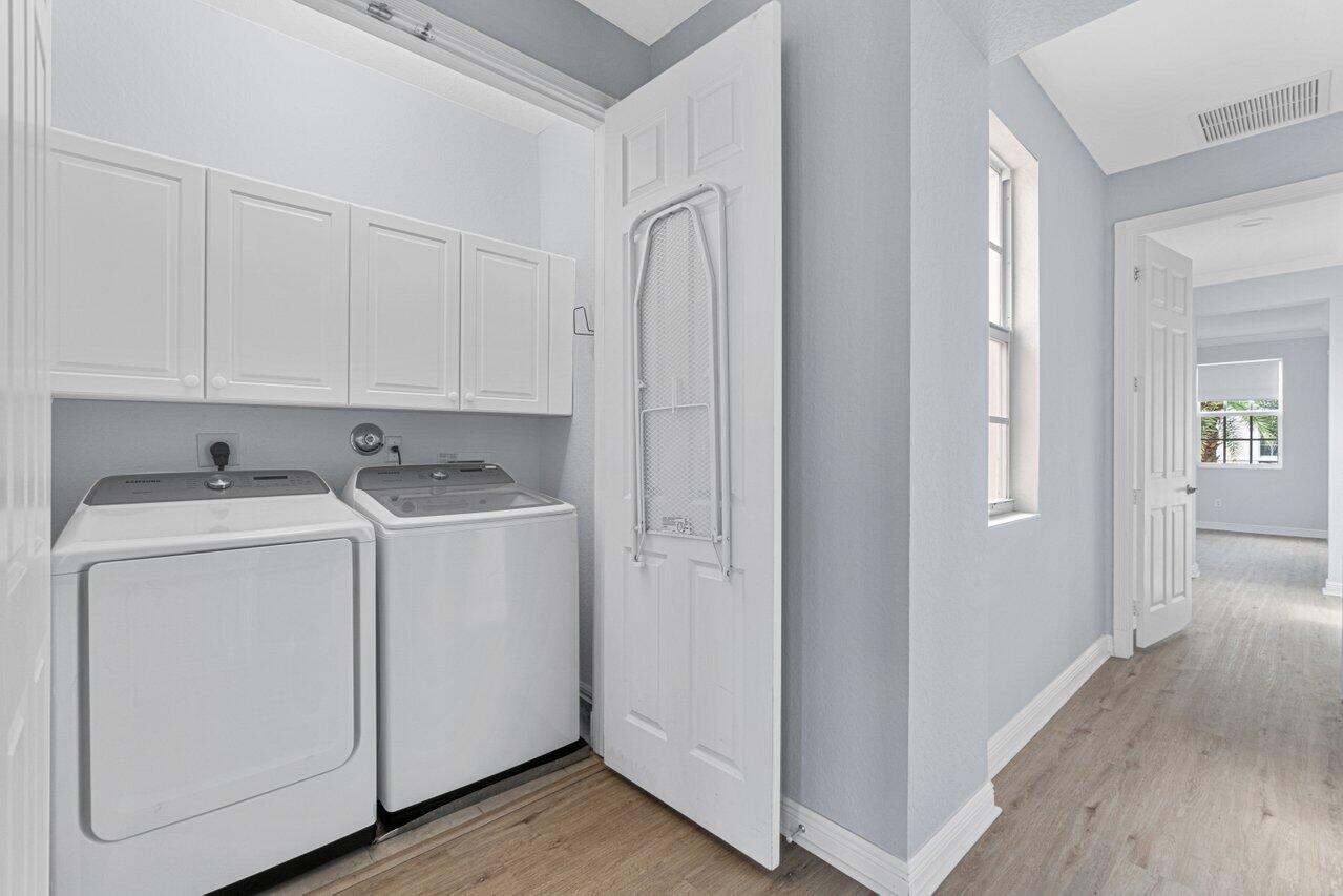 Laundry room with washer, dryer, overhead cabinets, and an ironing board beside a hallway.