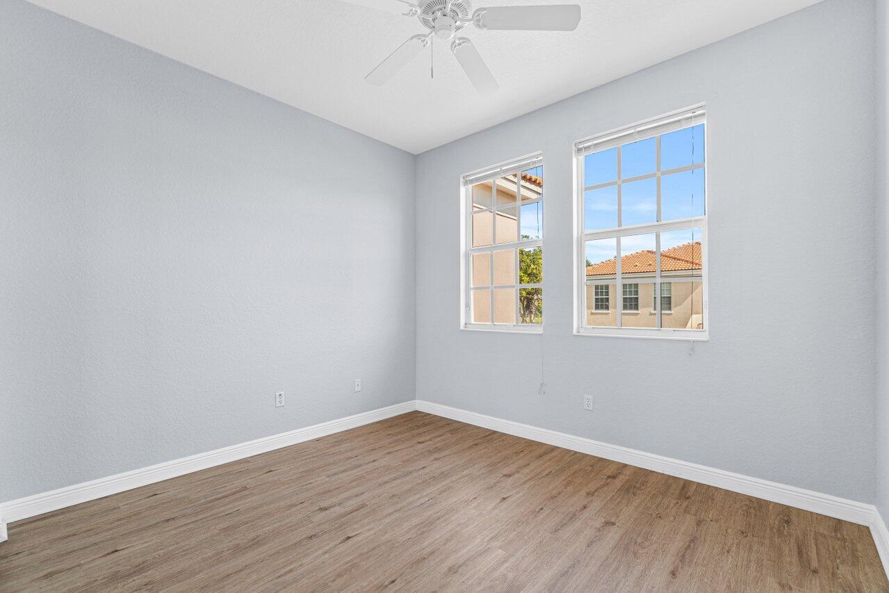 Empty room with wood-look flooring, two windows, and a ceiling fan.
