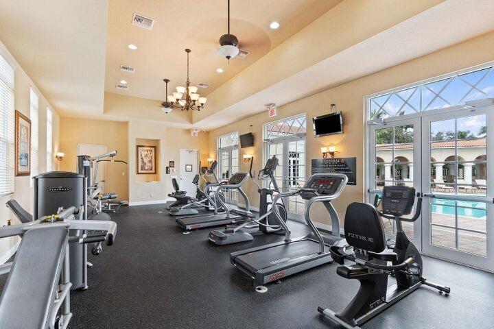 Fitness room with treadmills and weight machines, overlooking a pool through large windows.