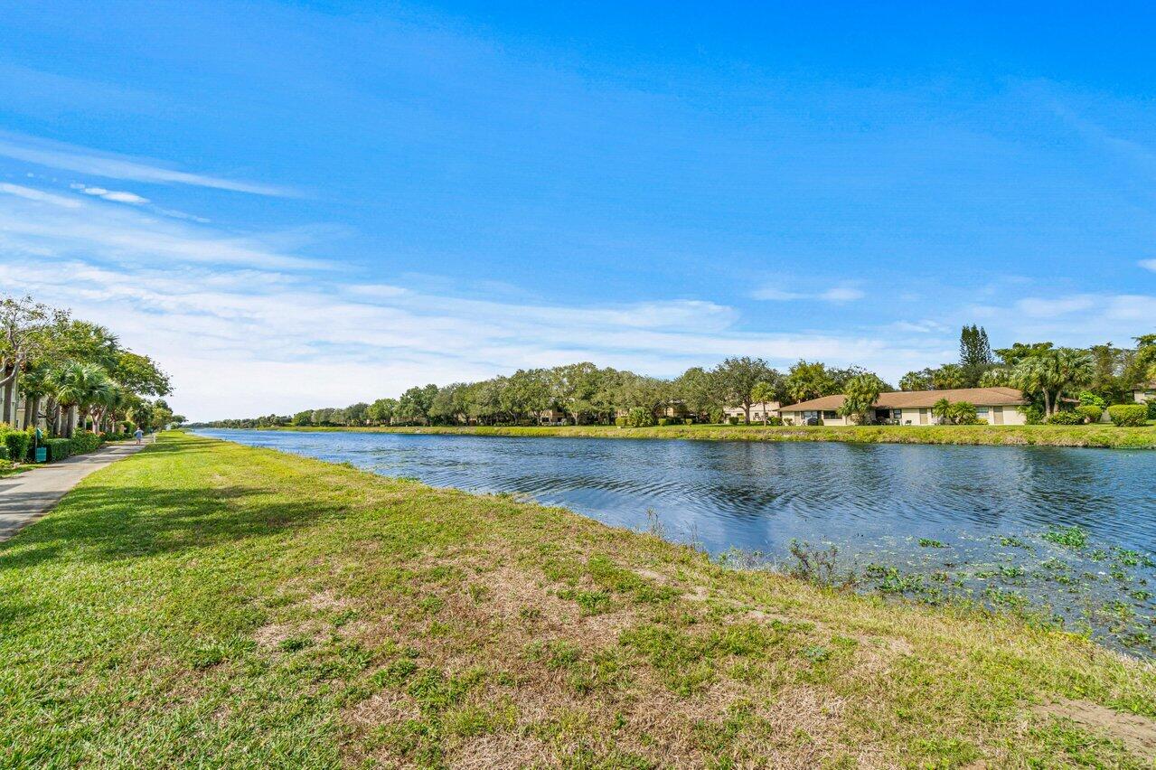 Residential canal with a grassy bank, paved walkway, and homes across the water.