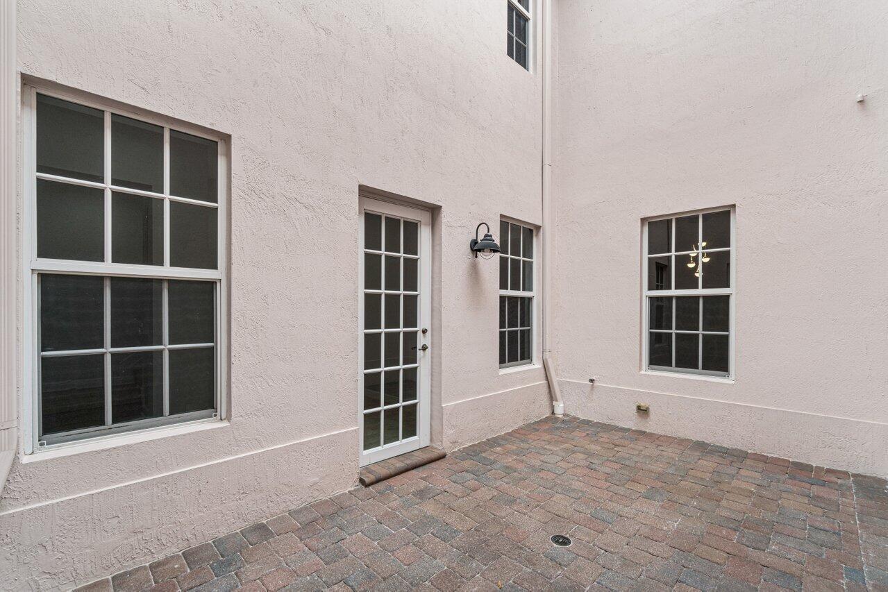 Paved courtyard beside a stucco home, with a glass-paneled door and white-framed windows.