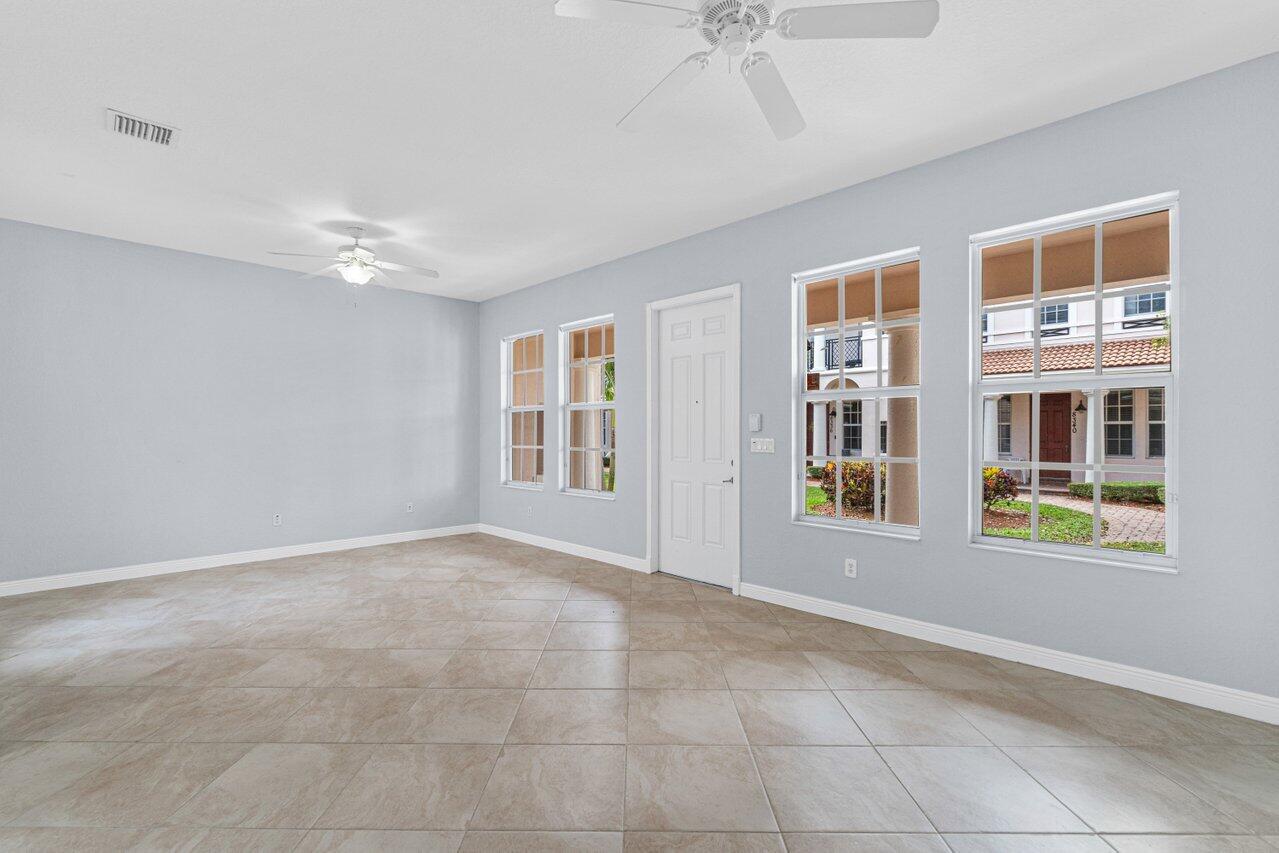 Empty tiled room with ceiling fans, large windows, and a white entry door.