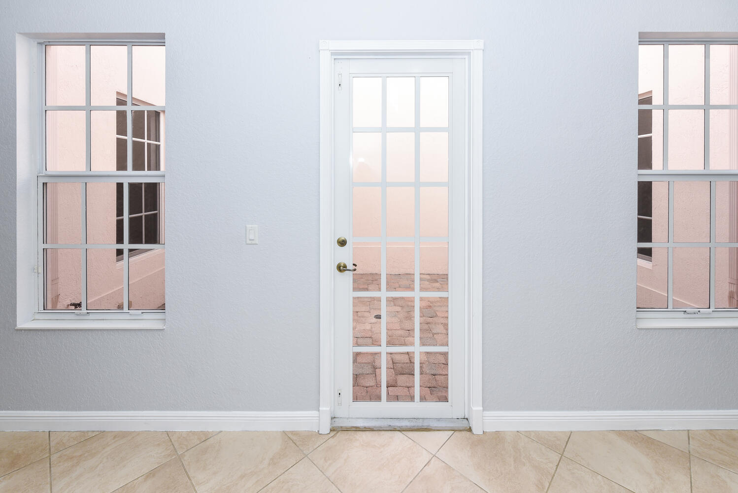 Glass patio door flanked by large grid-pane windows above beige tile flooring.