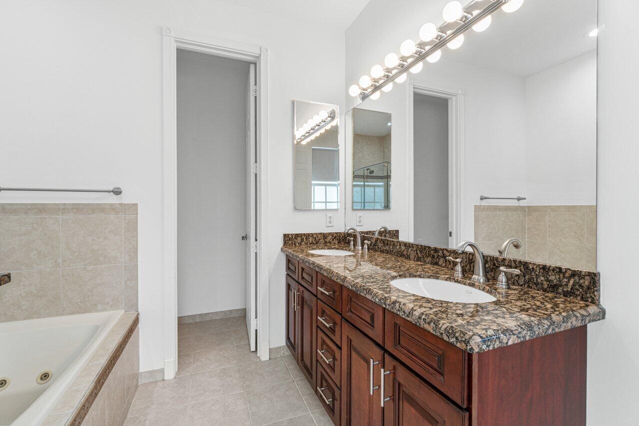 Bathroom with a double-sink granite vanity and a bathtub at the left.