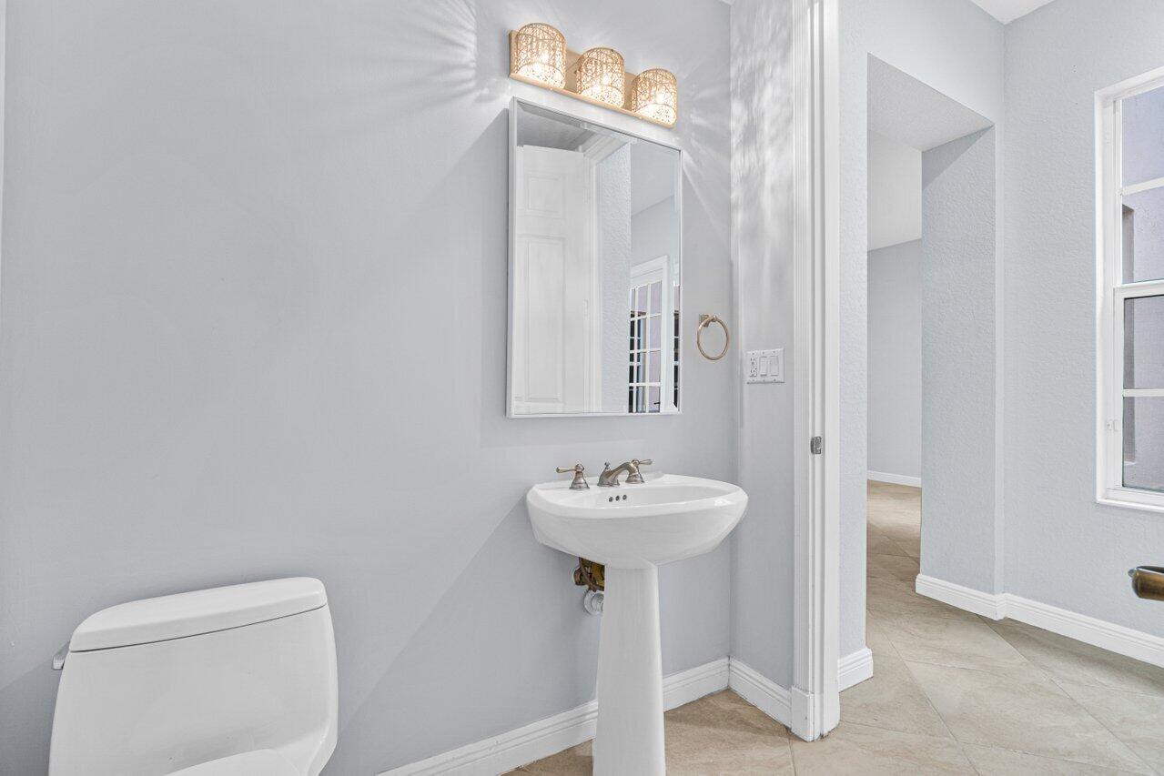 Bathroom with a white pedestal sink, rectangular mirror, and toilet beside an open doorway.
