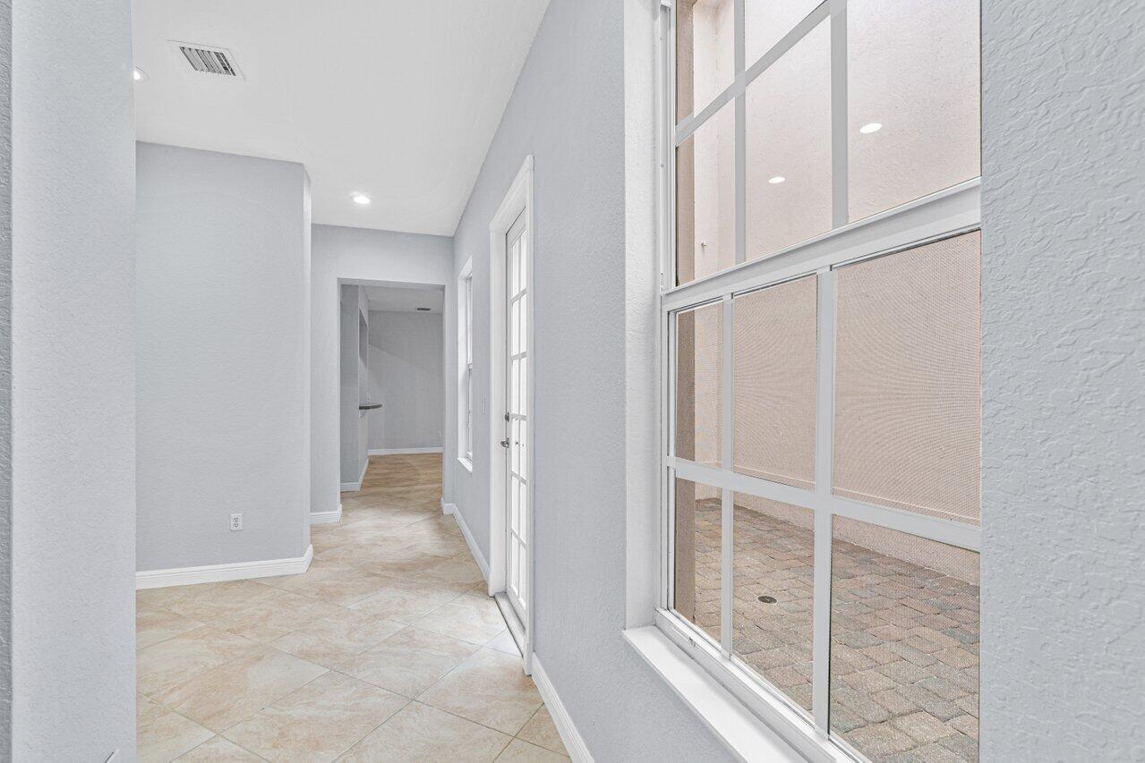 Bright tiled hallway with a large window overlooking a brick-paved screened patio.