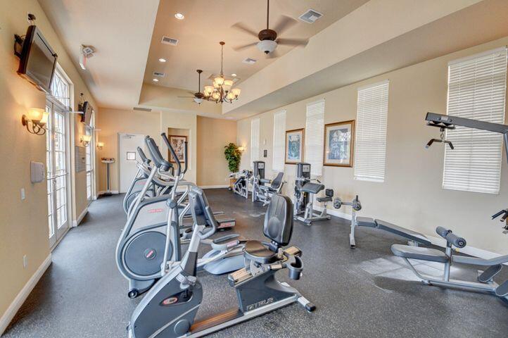 Fitness room with elliptical machines, stationary bikes, and weight equipment beside tall windows.