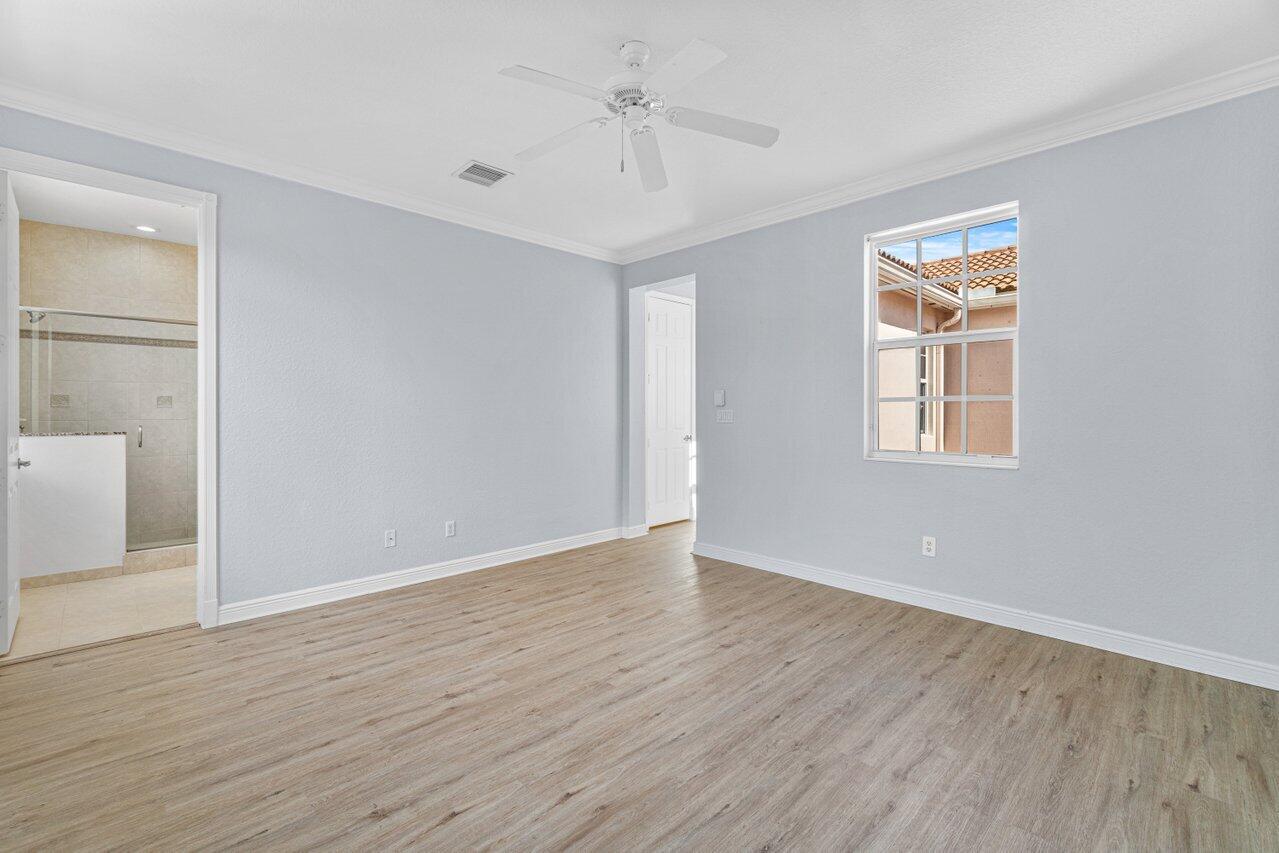 Empty bedroom with wood-look flooring, ceiling fan, and an open doorway to the tiled bathroom.