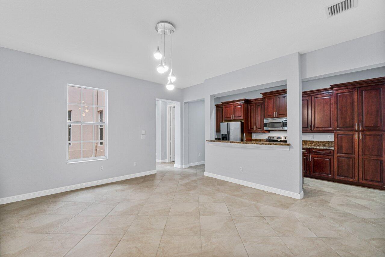Empty dining area opens to a kitchen with dark wood cabinets and beige tile floors.