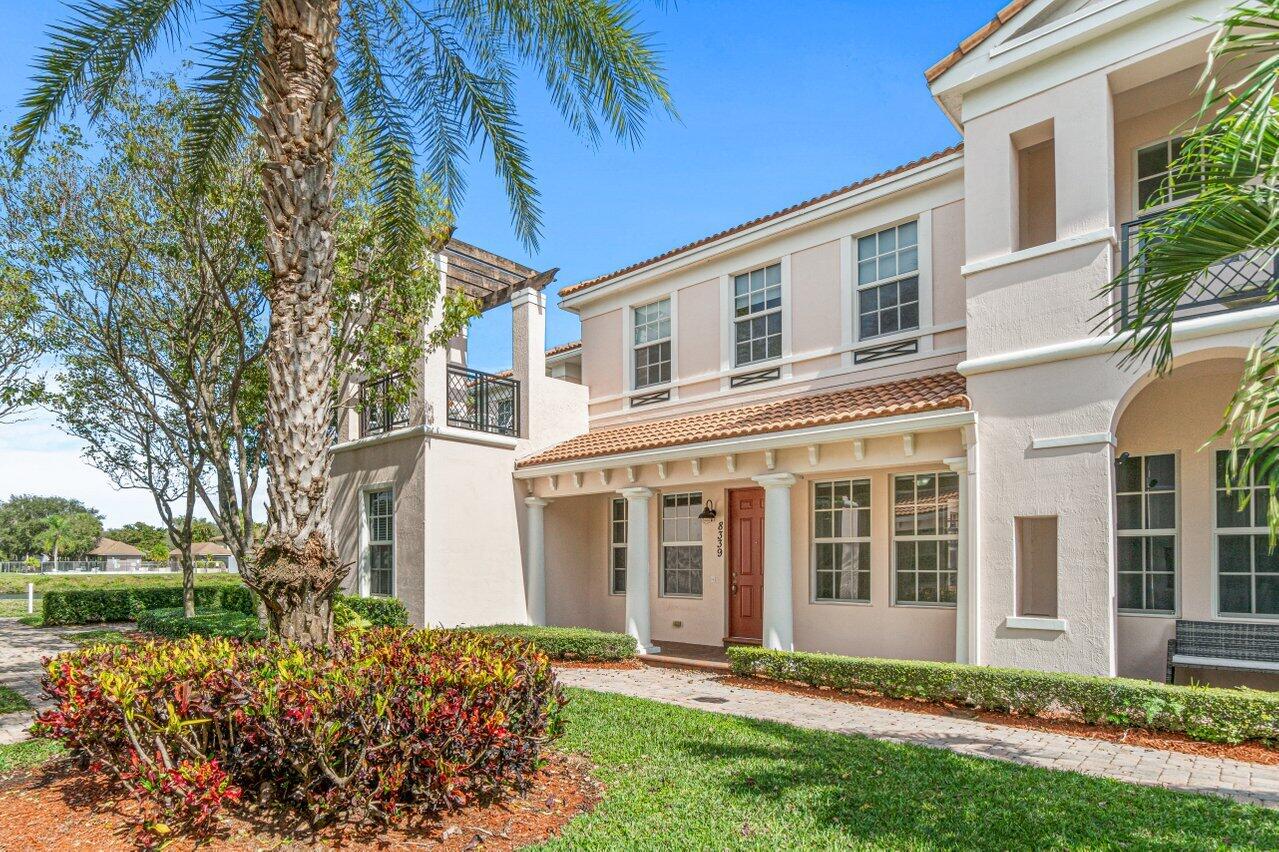 Two-story stucco home with a red front door, tile roof, and palm trees.