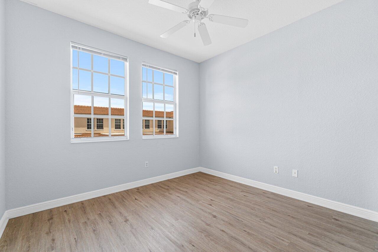 Empty room with two tall windows, a ceiling fan, and wood-look plank flooring.
