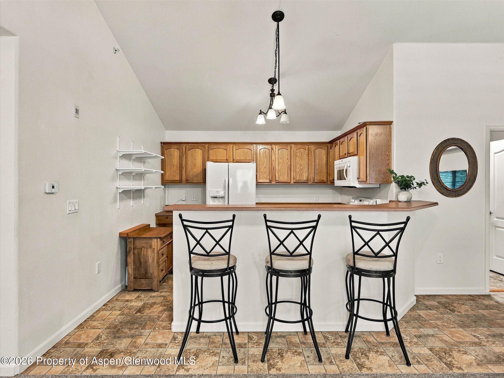 Kitchen with wood cabinets, a breakfast bar, and three black stools.
