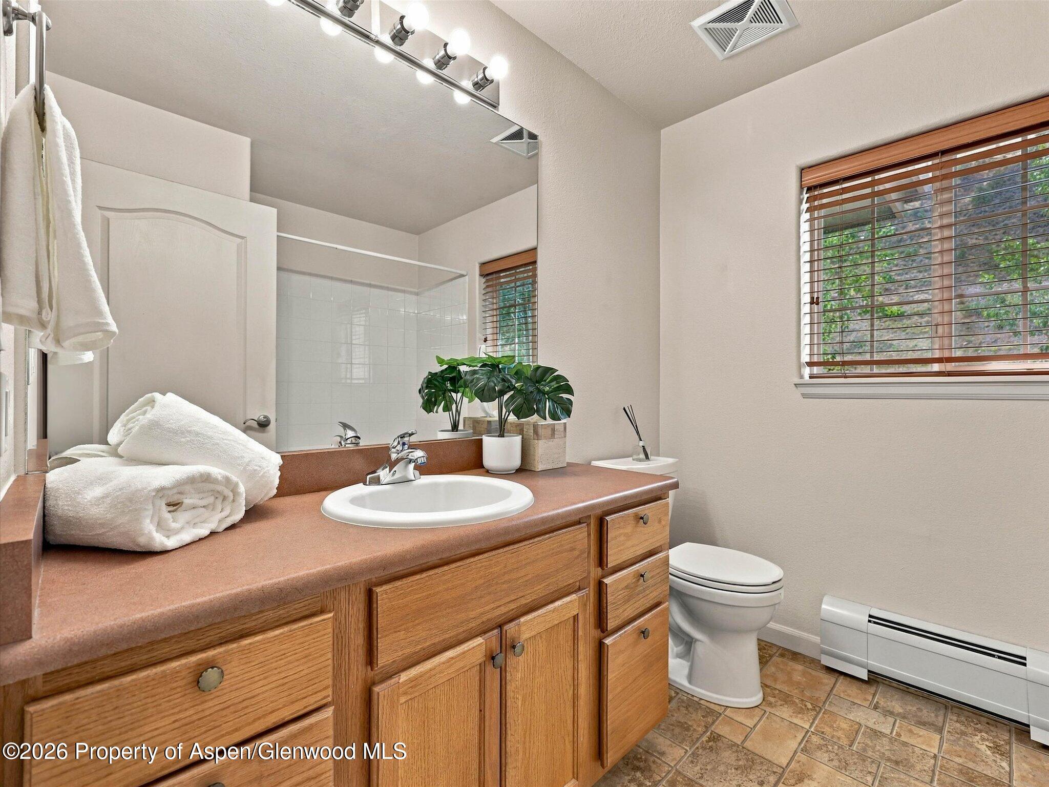 Bathroom with a wood vanity, large mirror, folded towels, and a window with wooden blinds.