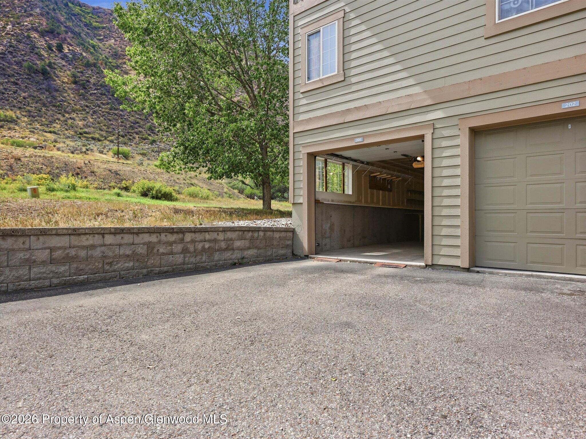 Building exterior with unit 206’s open garage, a neighboring closed garage, and a mountain hillside.