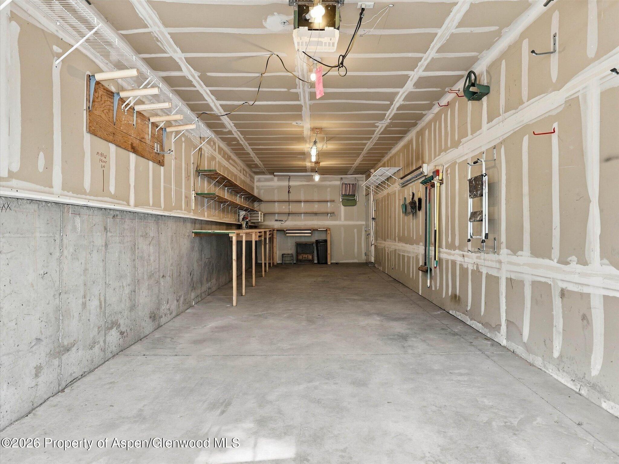 Empty garage with unfinished drywall, overhead storage racks, wall hooks, and a workbench.